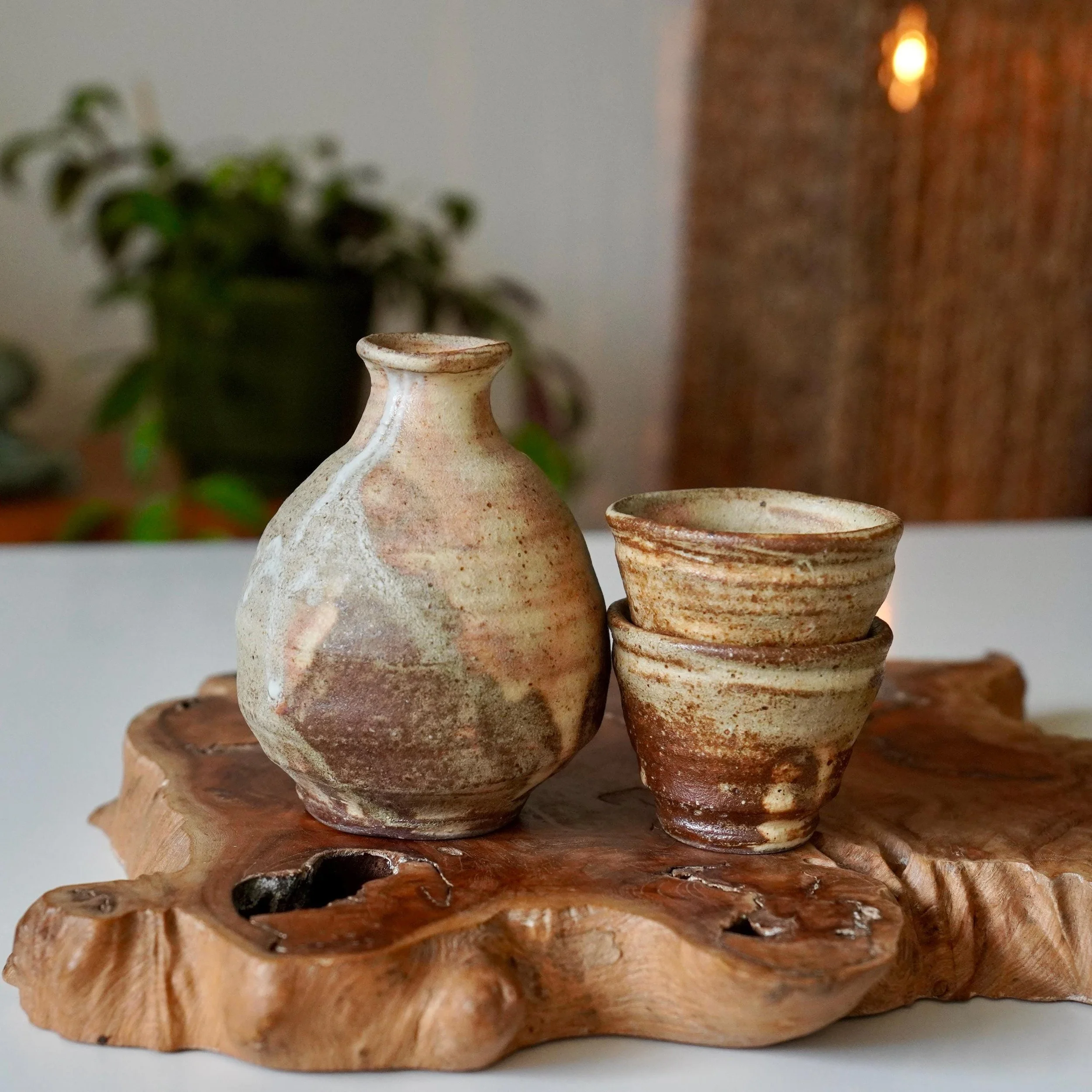 Wood-fired stoneware sake set tokkuri and two guinomi natural ash glaze, Shōwa period Japan, displayed on wooden plank, cups stacked