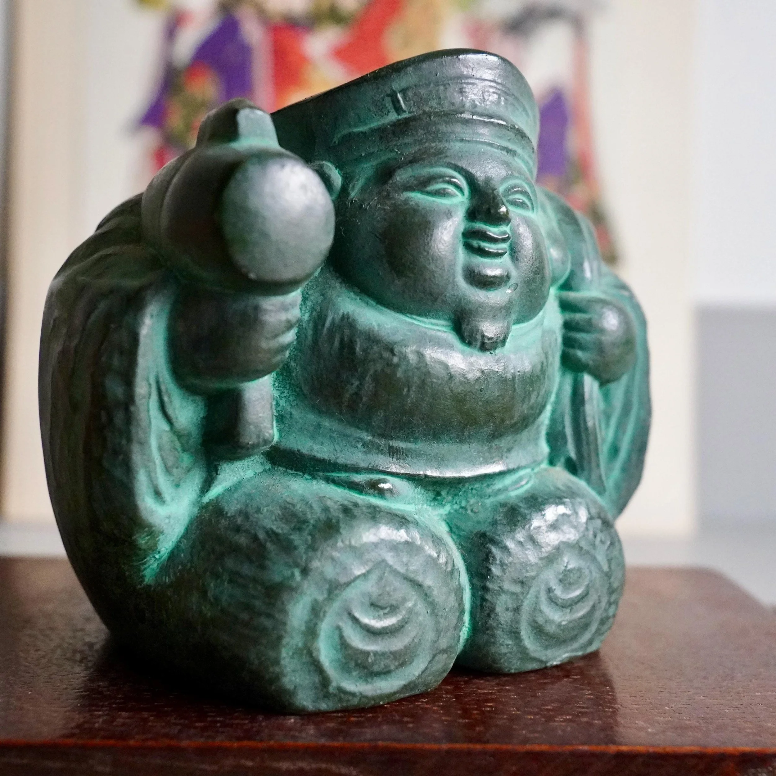 Close-up of two rice bales beneath Daikokuten bronze figure showing cast rope binding detail, symbol of abundance and wealth, green aged patina Showa period Japan