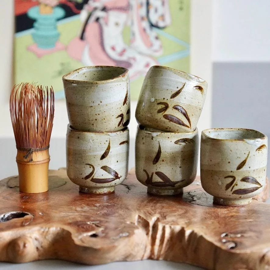 E-Karatsu yunomi set of five with hand-painted bamboo motif Maehira Tōgeien displayed on wooden plank ukiyoe print in background, late Shōwa period Japan, next to chasen whisk