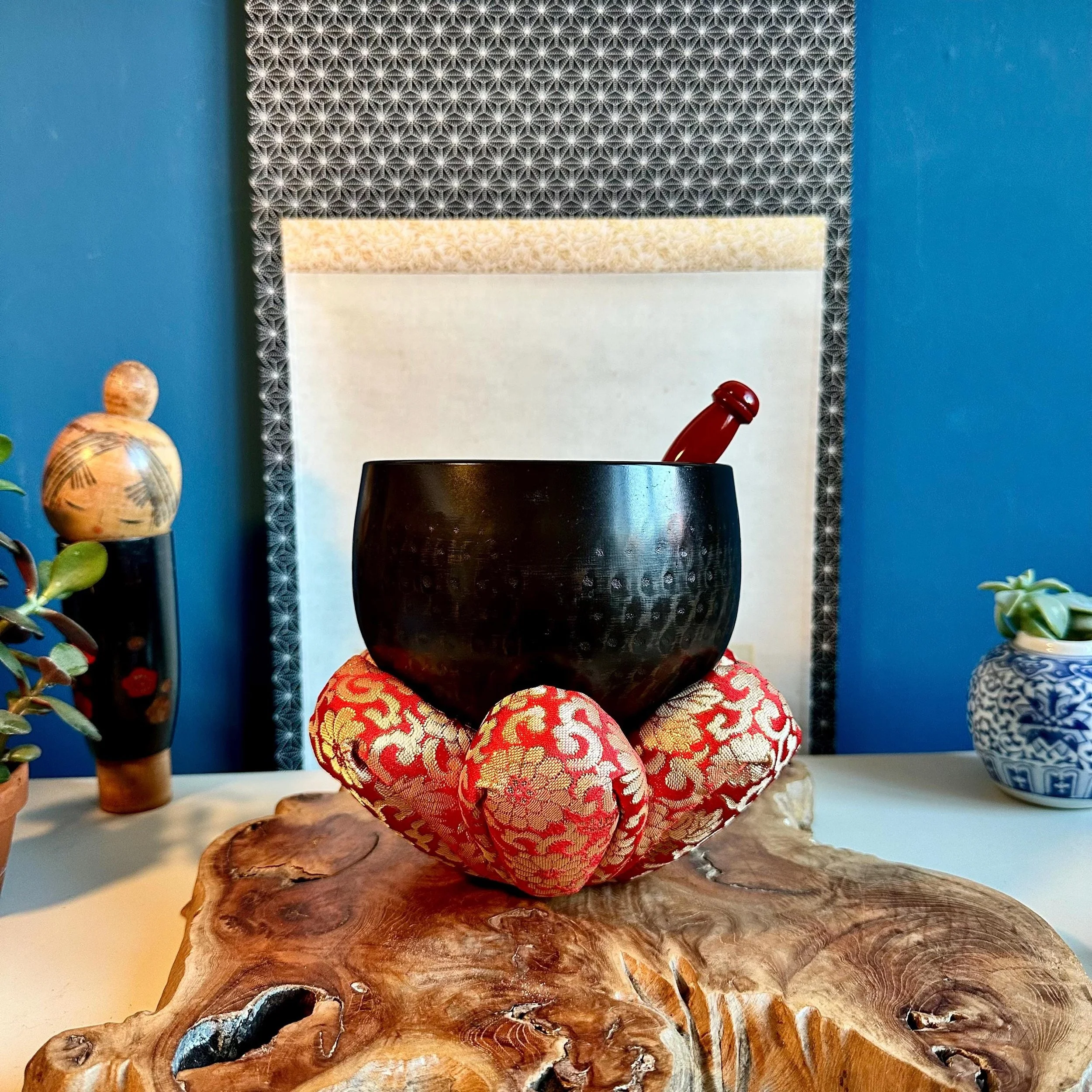 Vintage Japanese orin singing bowl hand-hammered tsuchime bronze on red and gold brocade zabuton cushion with wooden striker, kokeshi and kakejiku scroll in background, Shōwa period Japan