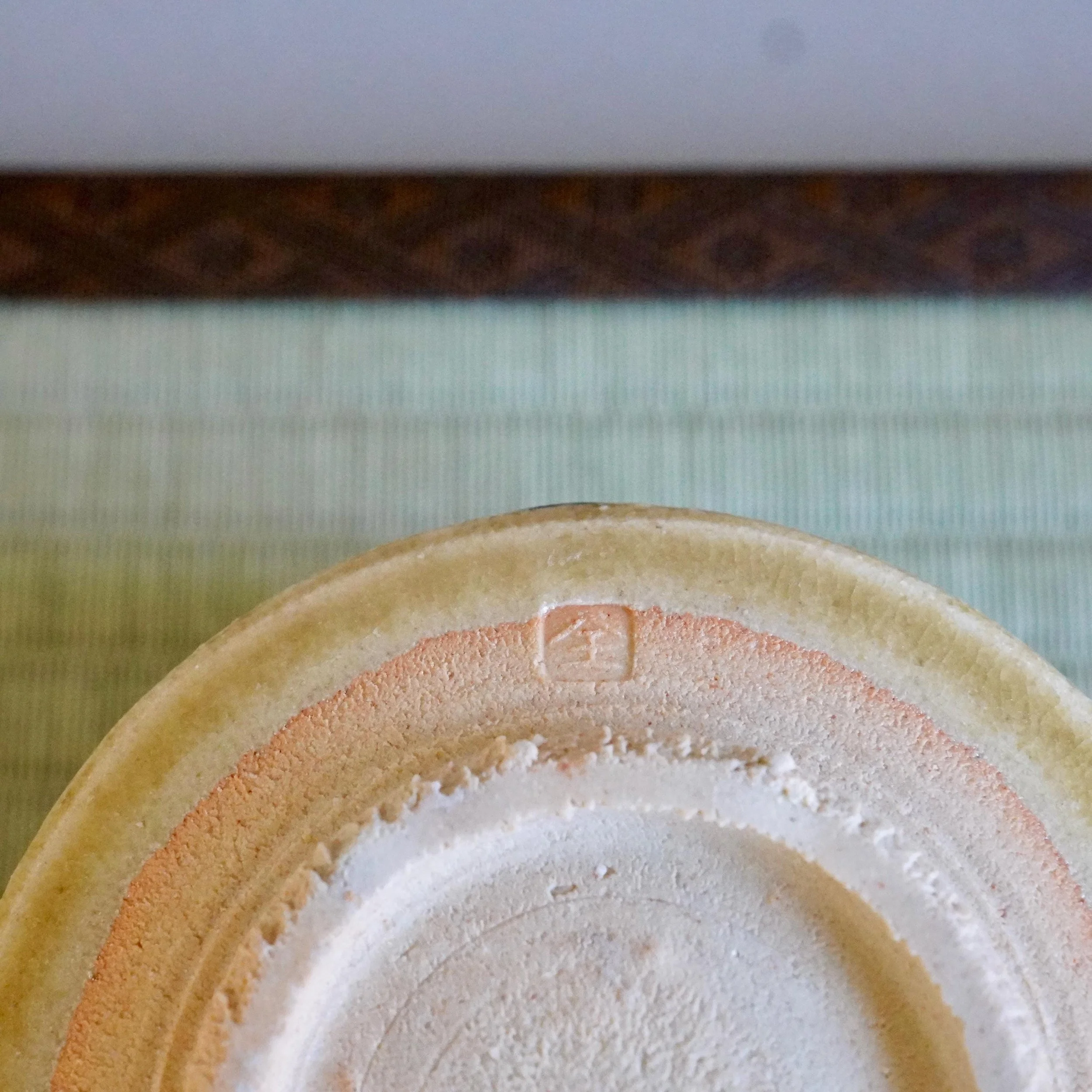Close-up of a chawan's footring by Yasuda Masahiro, featuring an impressed seal on beige clay with subtle reddish hues and a textured surface.