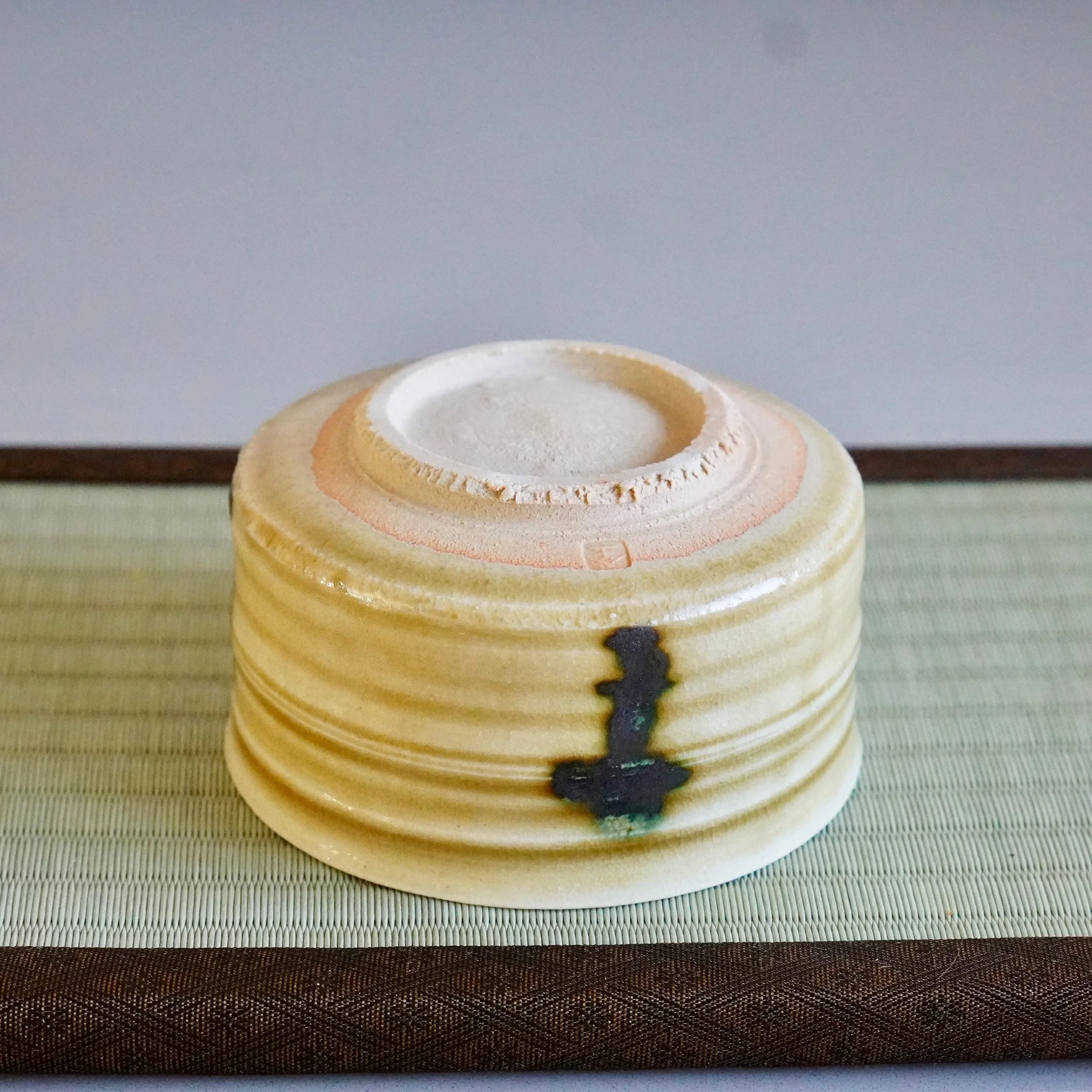 Upside-down Ki-Seto chawan by Yasuda Masahiro, its mustard-yellow body with horizontal ridges and a prominent dark green glaze drip, resting on a tatami mat.