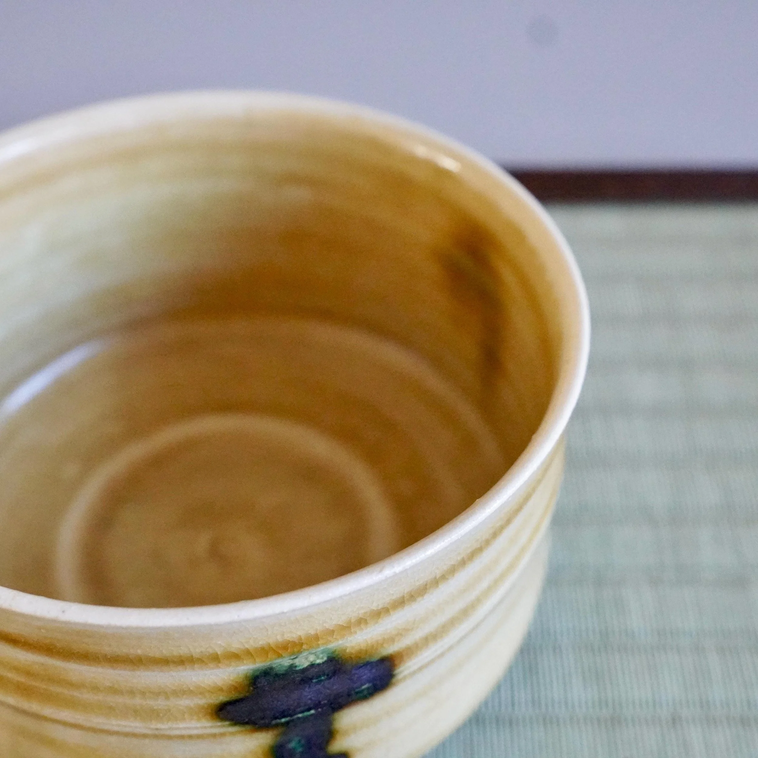 Yasuda Masahiro's Ki-Seto chawan, a mustard-yellow bowl with horizontal ridges and fine craquelure, and a dark green glaze drip. Interior and partial exterior view.