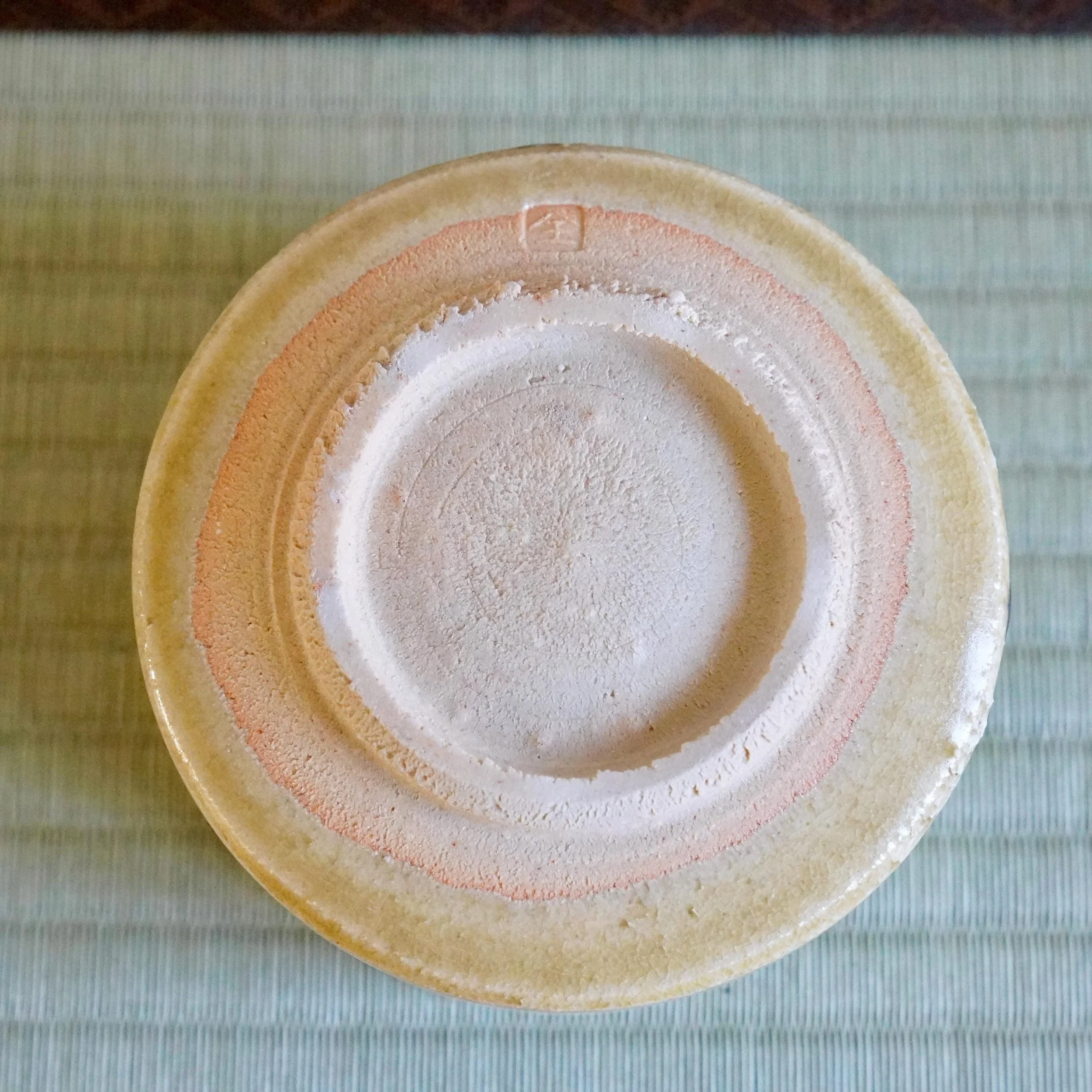 Underside of a Ki-Seto chawan by Yasuda Masahiro, displaying the raw clay foot with an impressed seal and crackled yellow-beige glaze.