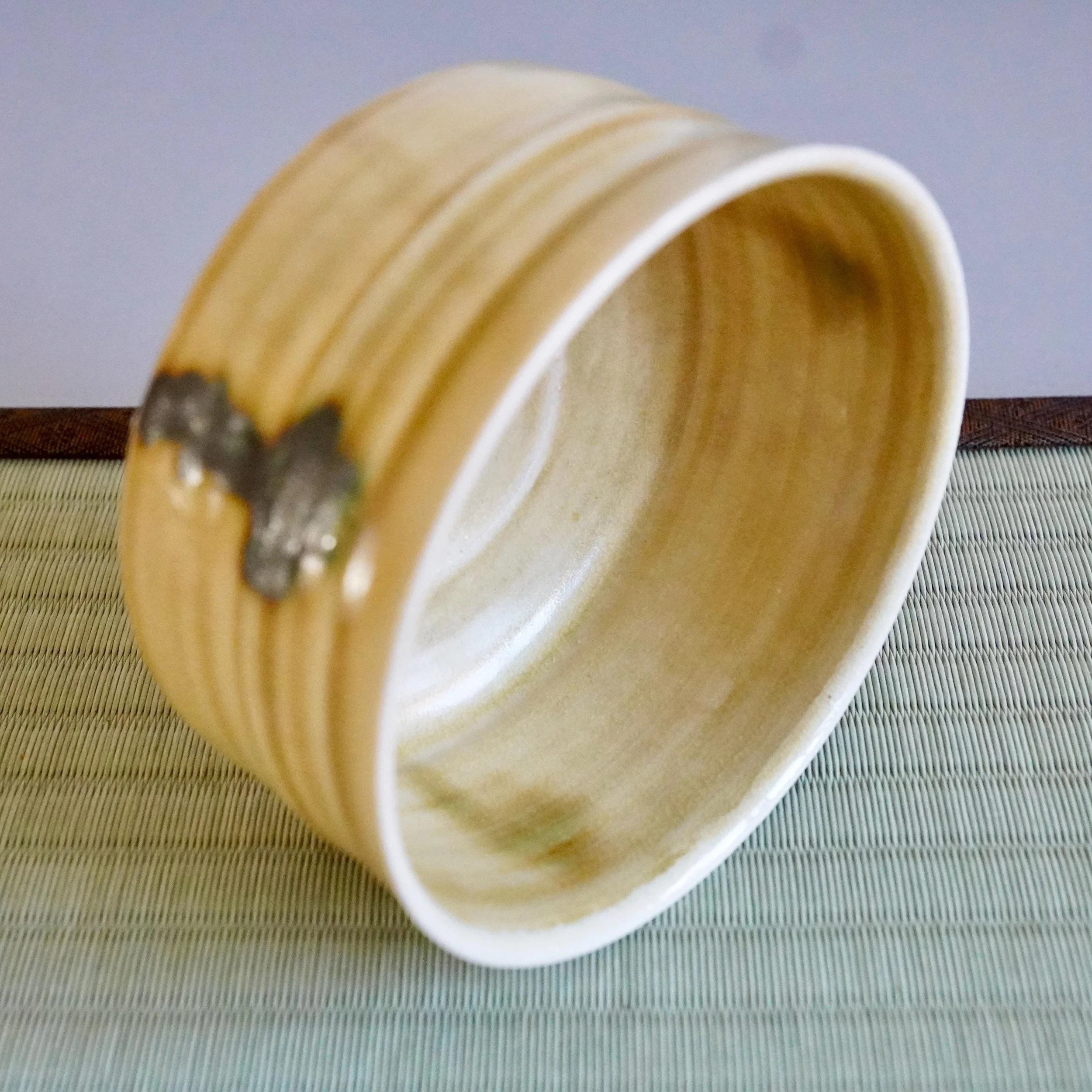 Yasuda Masahiro Ki-Seto chawan, mustard-yellow with horizontal ridges, featuring three dark green drips on its side, resting on a tatami mat.