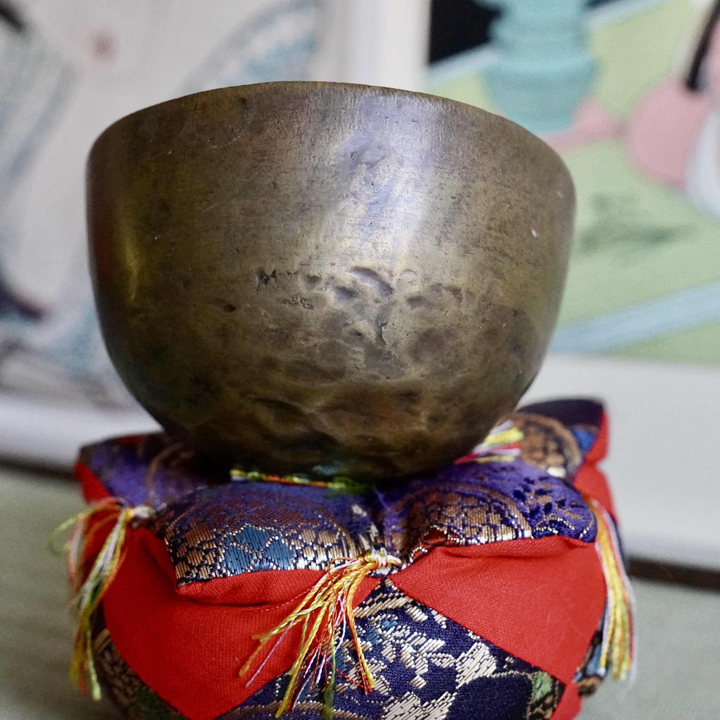 Front view of small bronze orin singing bowl on brocade cushion, tatami mat