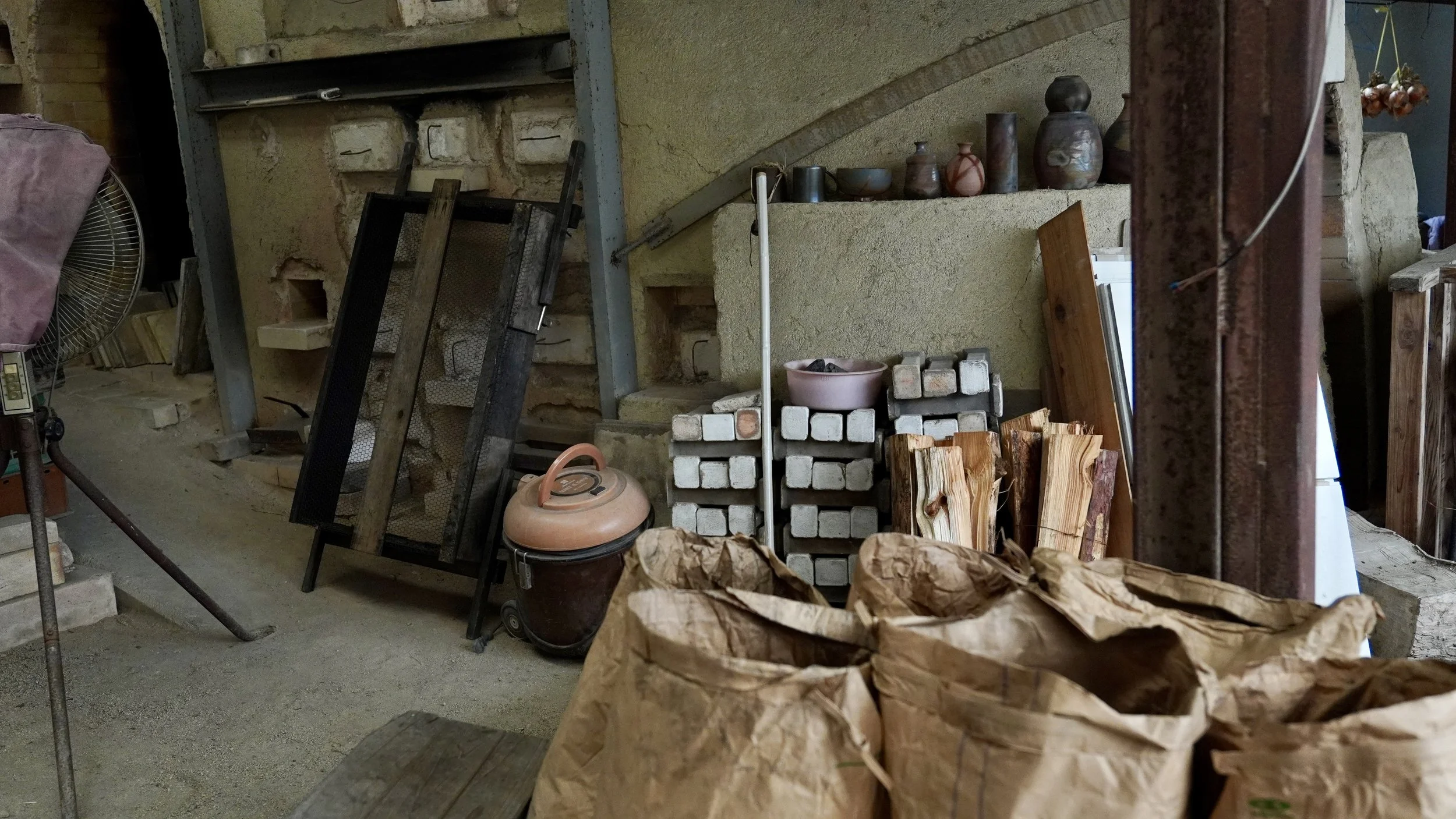 Stacked firewood and paper sacks of charcoal beside a noborigama kiln at Shibaoka Tōsendō pottery workshop, Imbe Okayama Japan