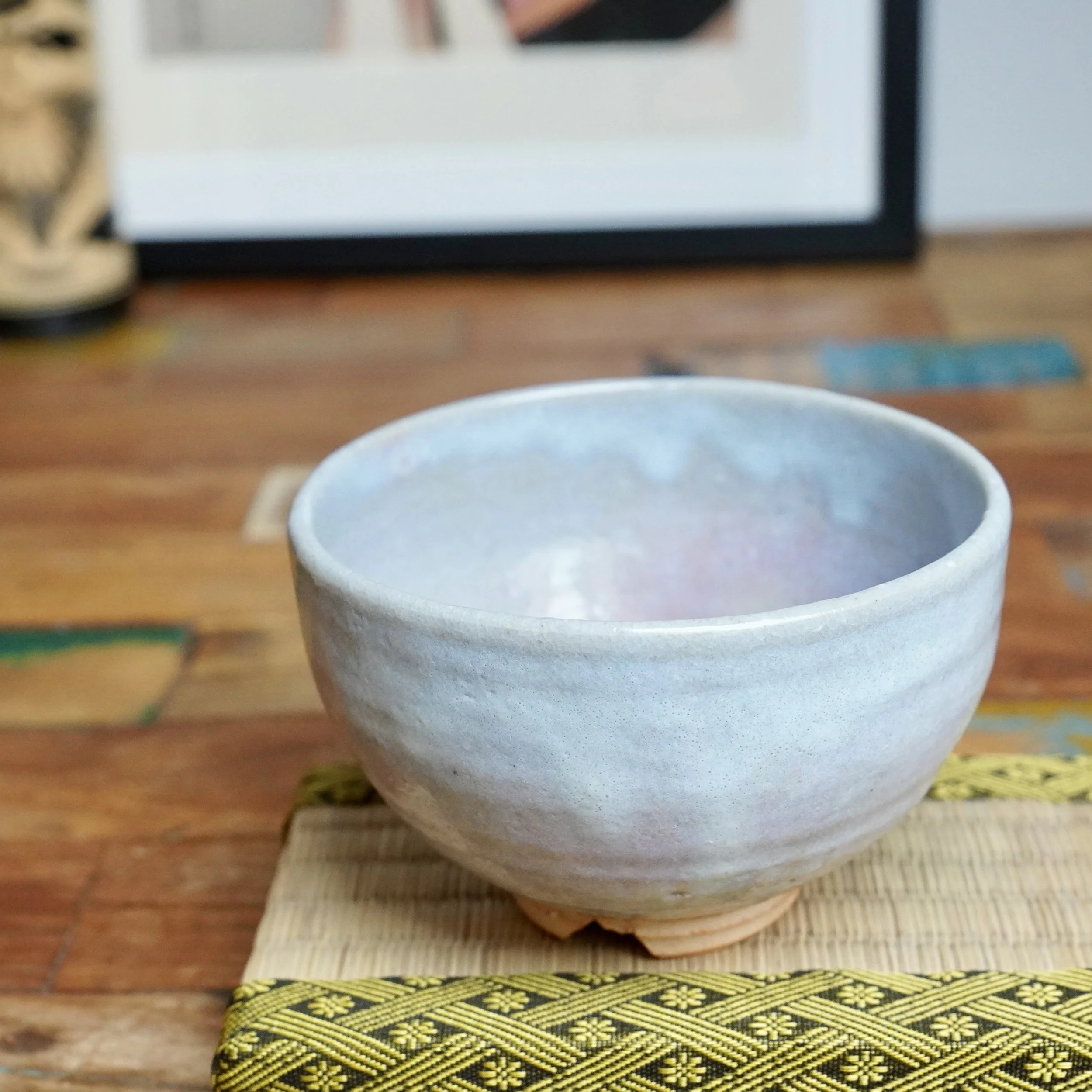 Hagi-yaki chawan by Moriwaki Fumitada, light blue-grey crackled glaze with hints of lilac, resting on a yellow patterned mat.