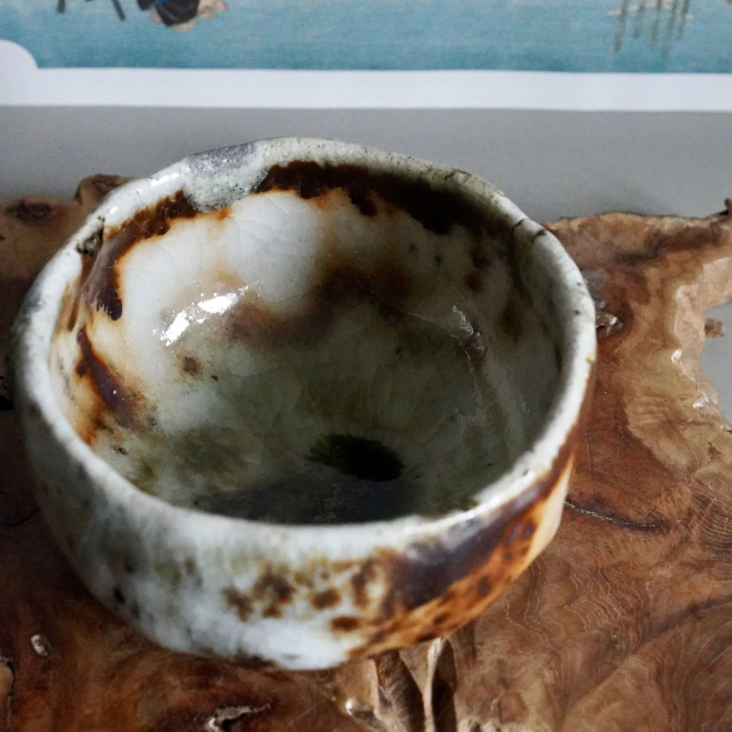 Deguchi Eiji chawan with a complex, wood-fired glaze. Its crackled white exterior transitions to rustic reddish-brown, while the interior is a deep mossy green. Resting on a textured wooden surface.