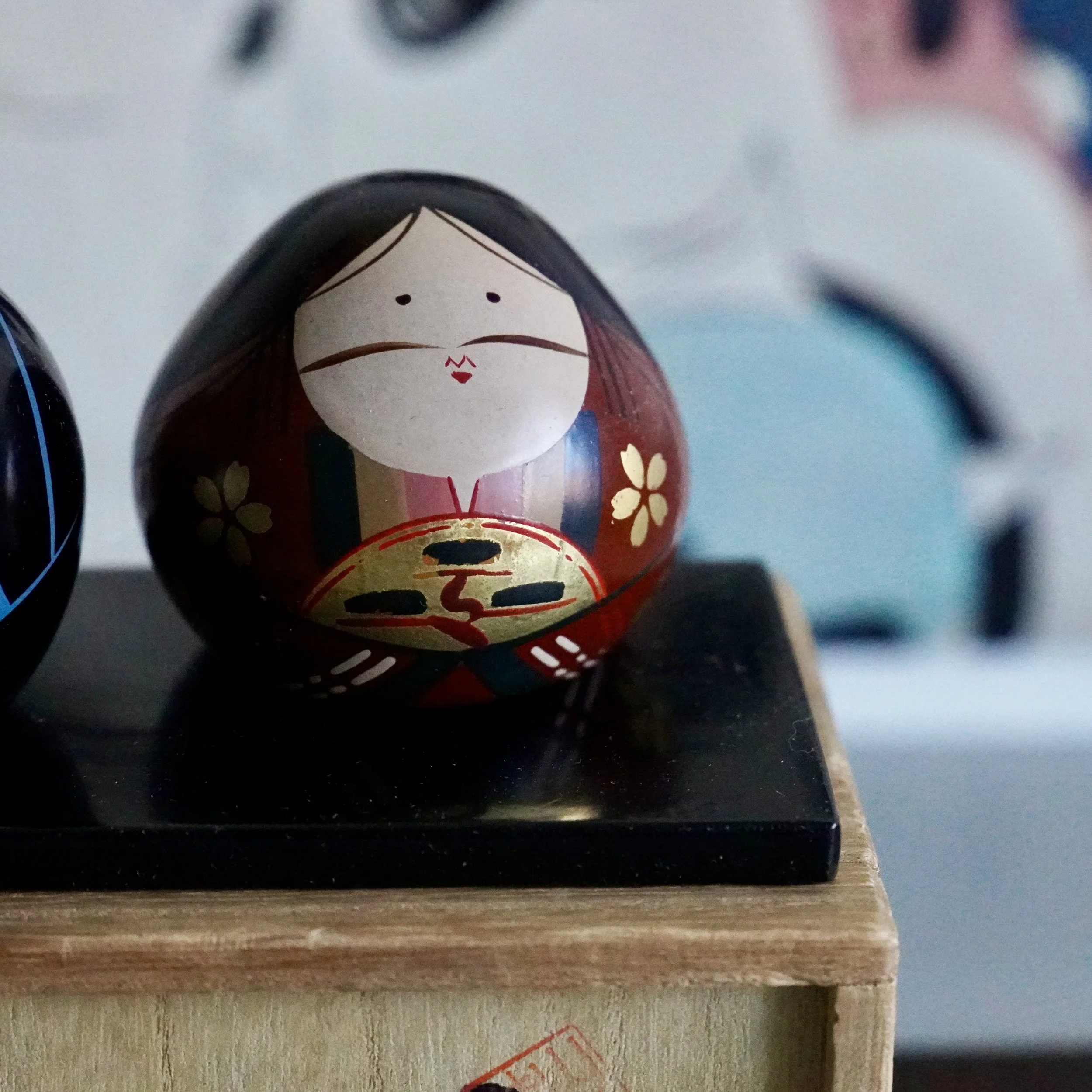 Ouchi-nuri hina doll pair close-up on tomobako lid, gold sakura and fan detail visible