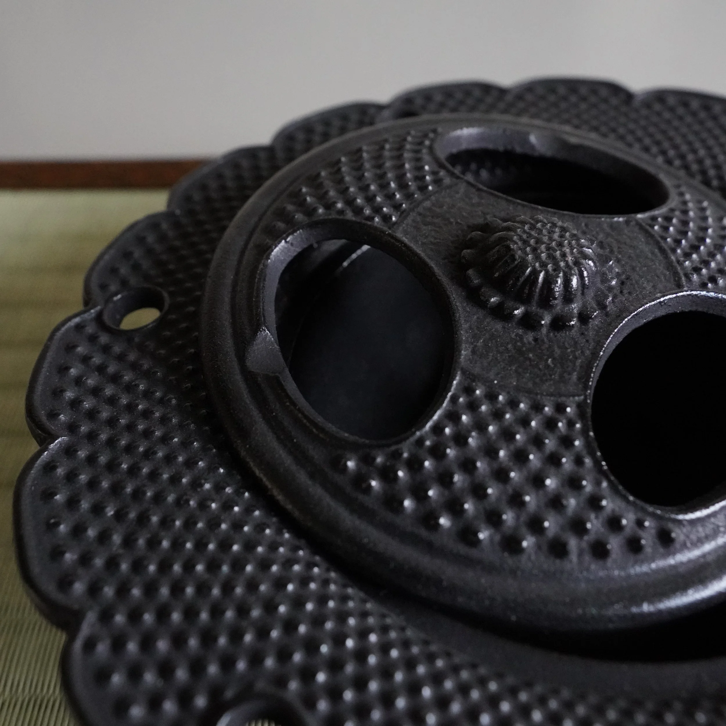 Detail of a cast iron sakura-shaped lid with three pierced holes and hobnail arare texture, Nanbu ironware Japan
