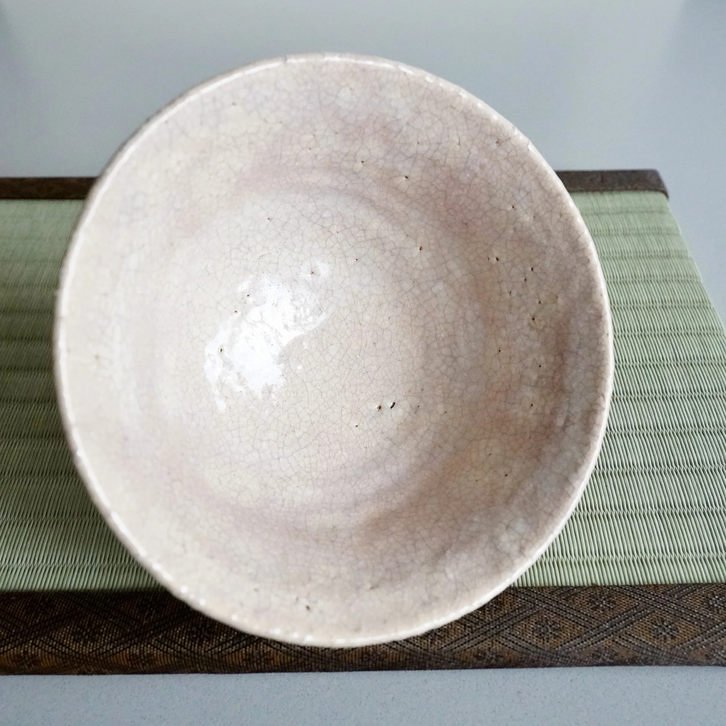 Overhead view of matcha chawan interior, pale crackled Hagi glaze with soft pink karahai glow