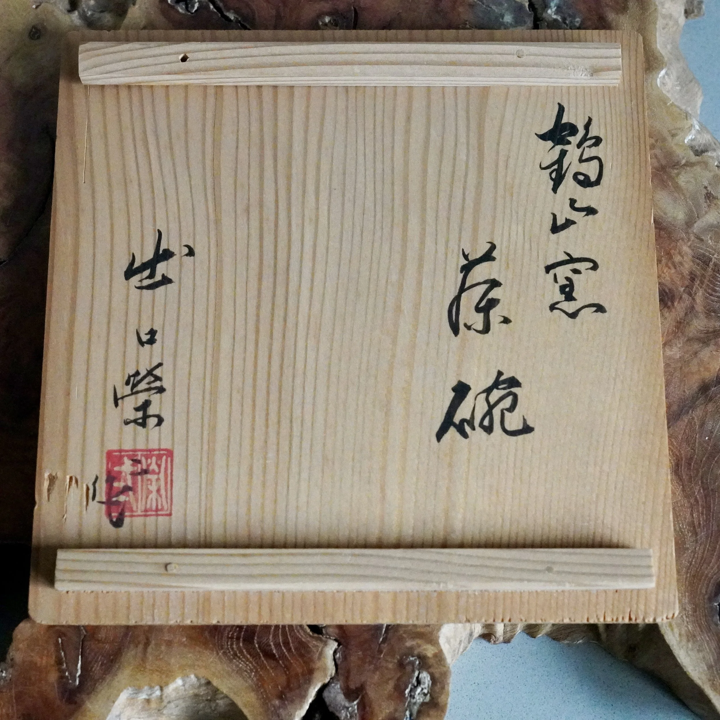Wooden tomobako with vertical grain and horizontal battens, inscribed in black calligraphy with "Kakuzan-gama original bowl" and "Deguchi Eiji", marked by a red seal.