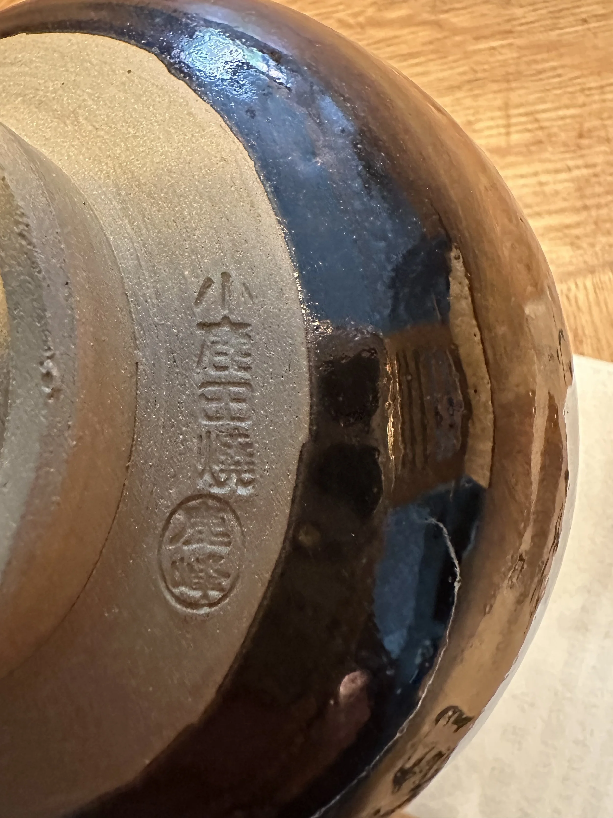 Detail of the underside of a Rokuhō ceramic bowl, showing the unglazed light brown clay foot with a carved 鹿峰 signature and dark brown-blue glaze.