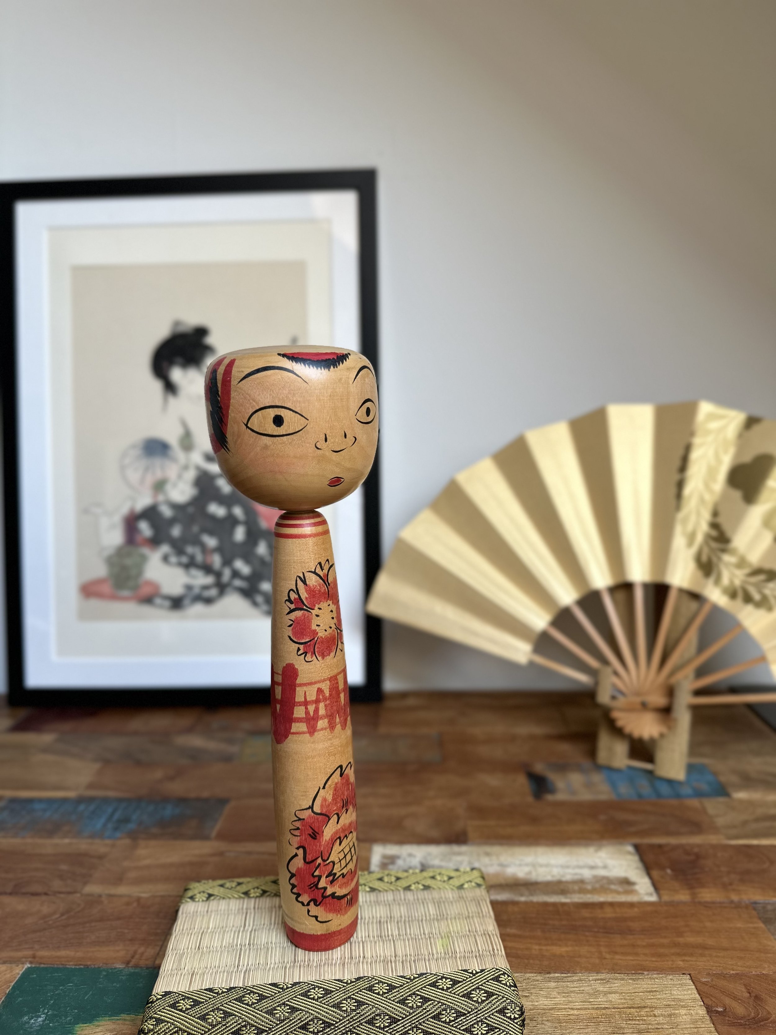 Seya Jūji's Nakanosawa Takobozu kokeshi has a wide, expressive painted face with eyes and red lips. Its slender body is decorated with red cherry blossoms.