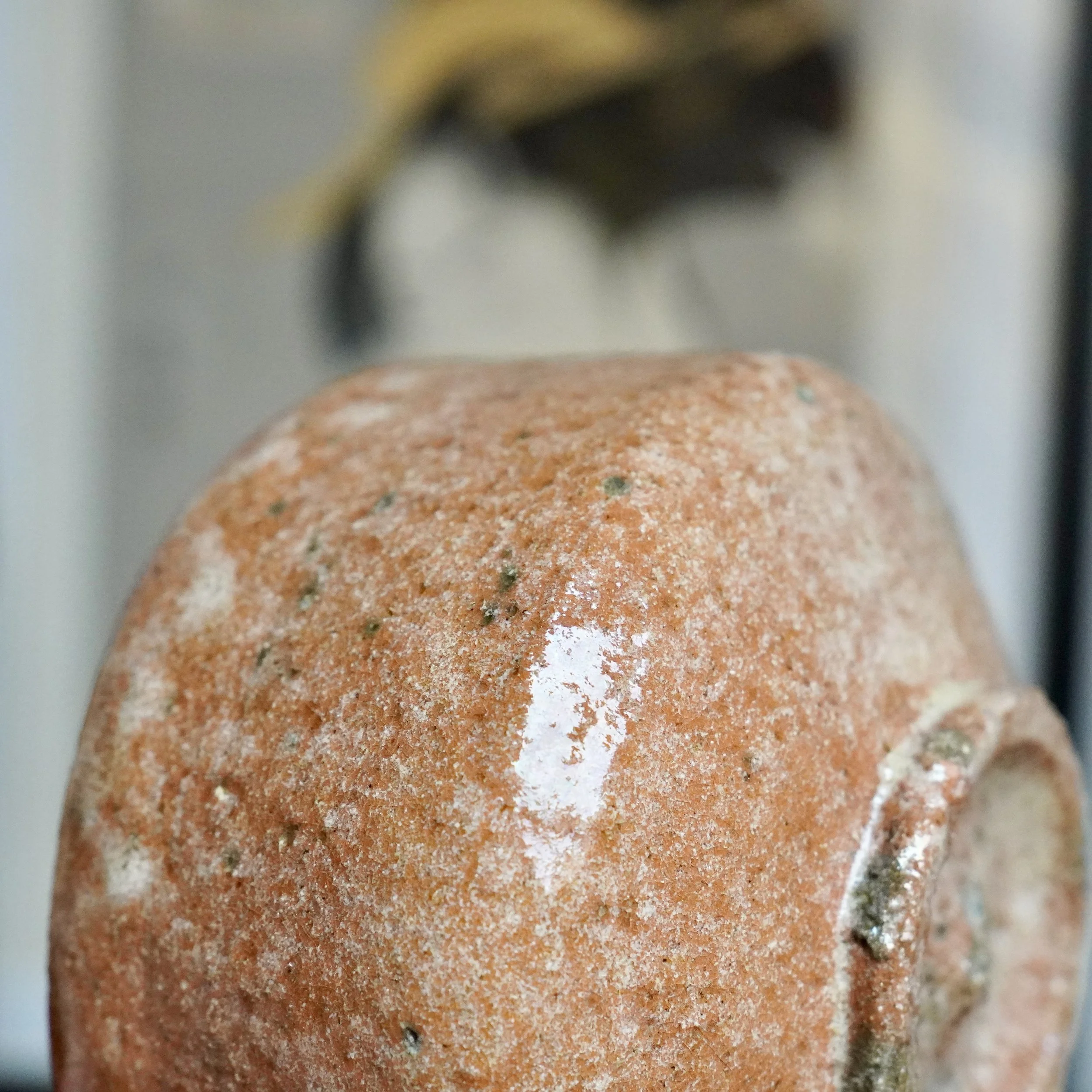 Sawada Hiroyuki's aka-raku chawan, a close-up of its rugged, sandy, reddish surface with white glaze dripping, glossy patches, and dark specks.