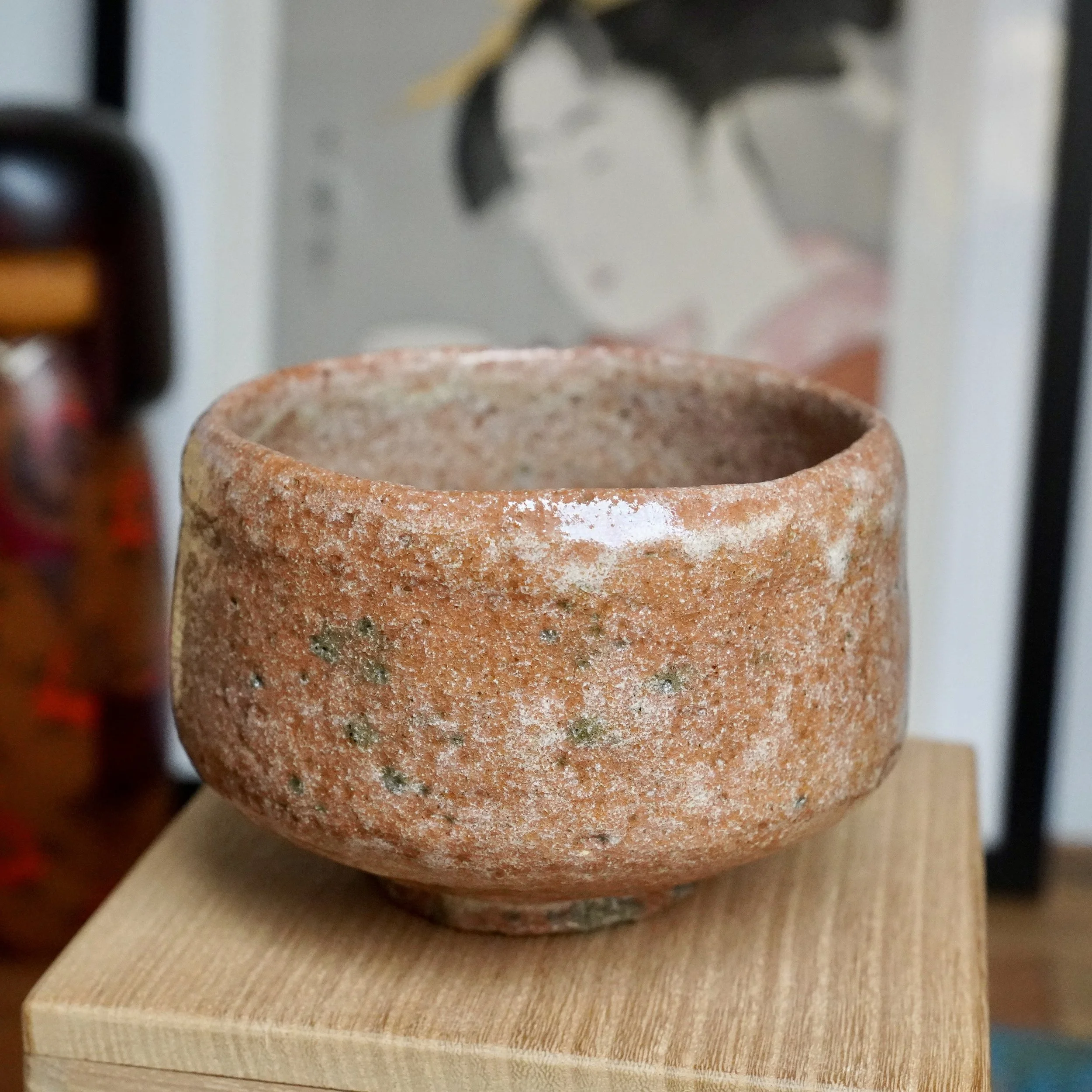 Aka-raku chawan by Sawada Hiroyuki, a rugged, terracotta-colored bowl with white glaze drips, glossy patches, and hints of green on its textured surface, resting on wood.