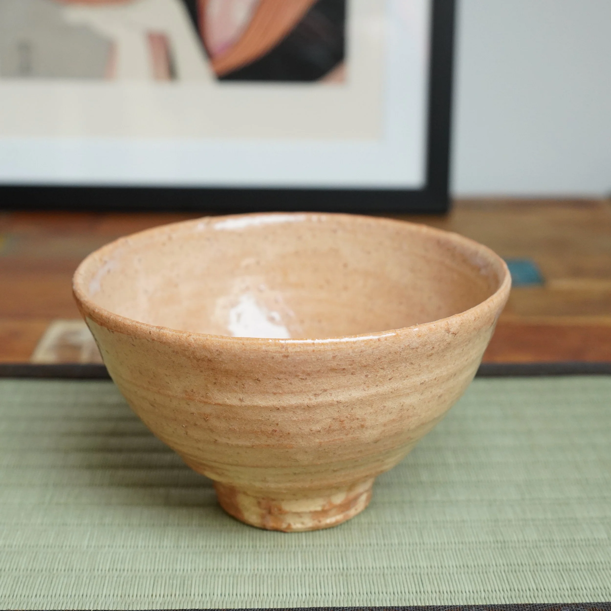Hagi-yaki chawan by Kaneko Nobuhiko, with a salmon pink to apricot body, visible throwing lines, iron freckles, and milky white glaze on the rim, sitting on a tatami mat.