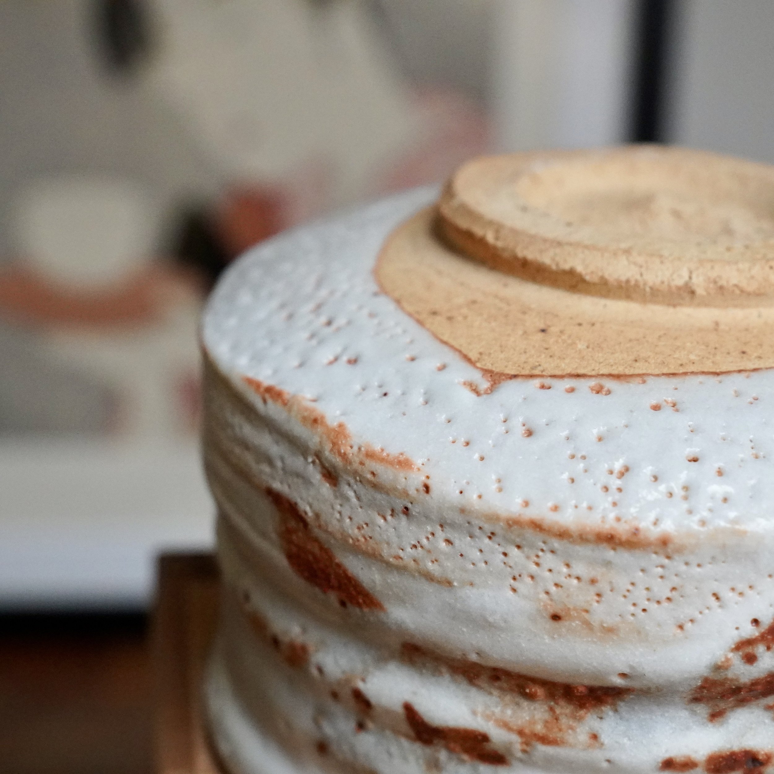 Shino chawan detail view, showing thick walls with textured white glaze, rust-orange blushes, and an unglazed tan circular foot on top.