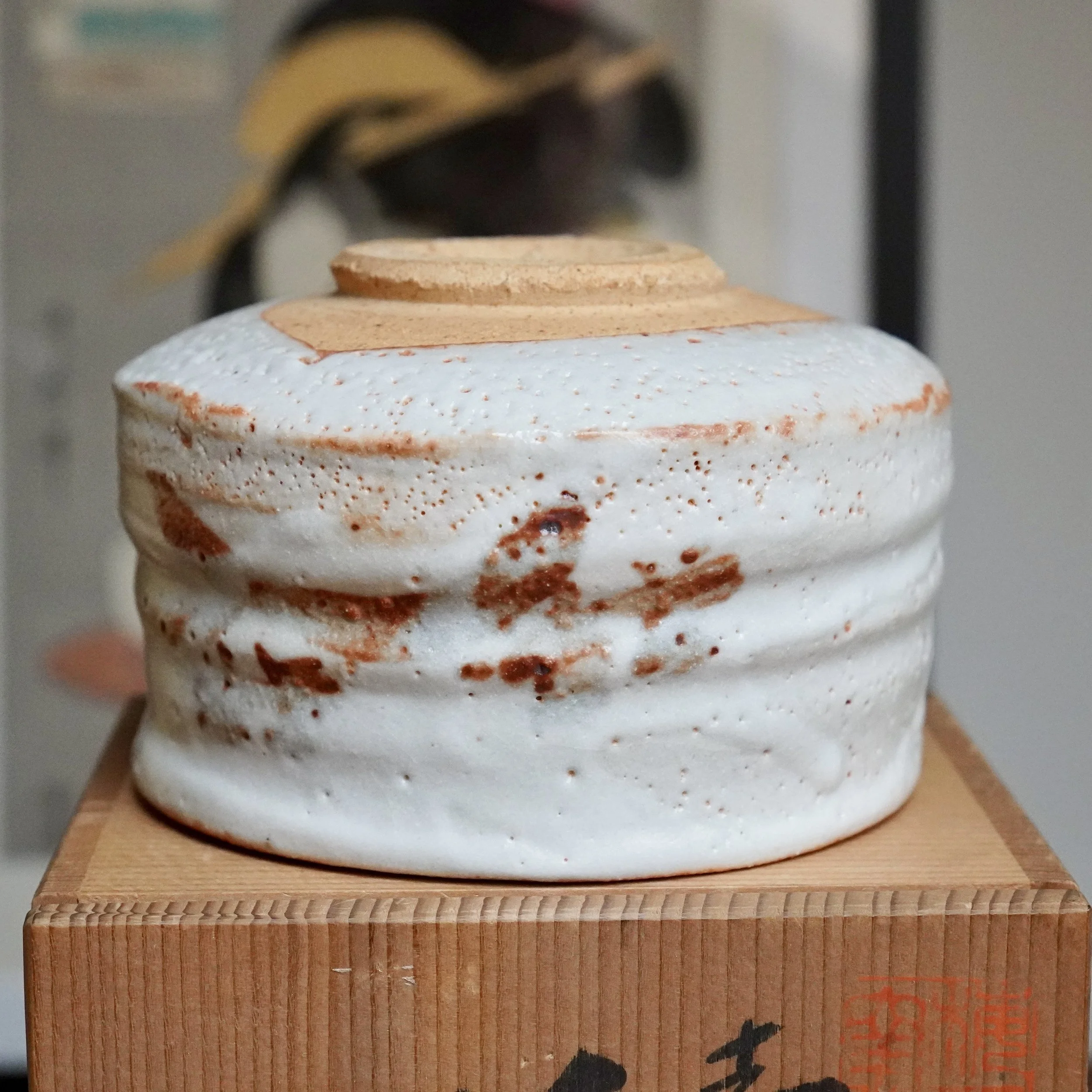 Textured Shino chawan with white glaze and rust-orange accents, resting on a signed wooden tomobako box with visible Japanese script.