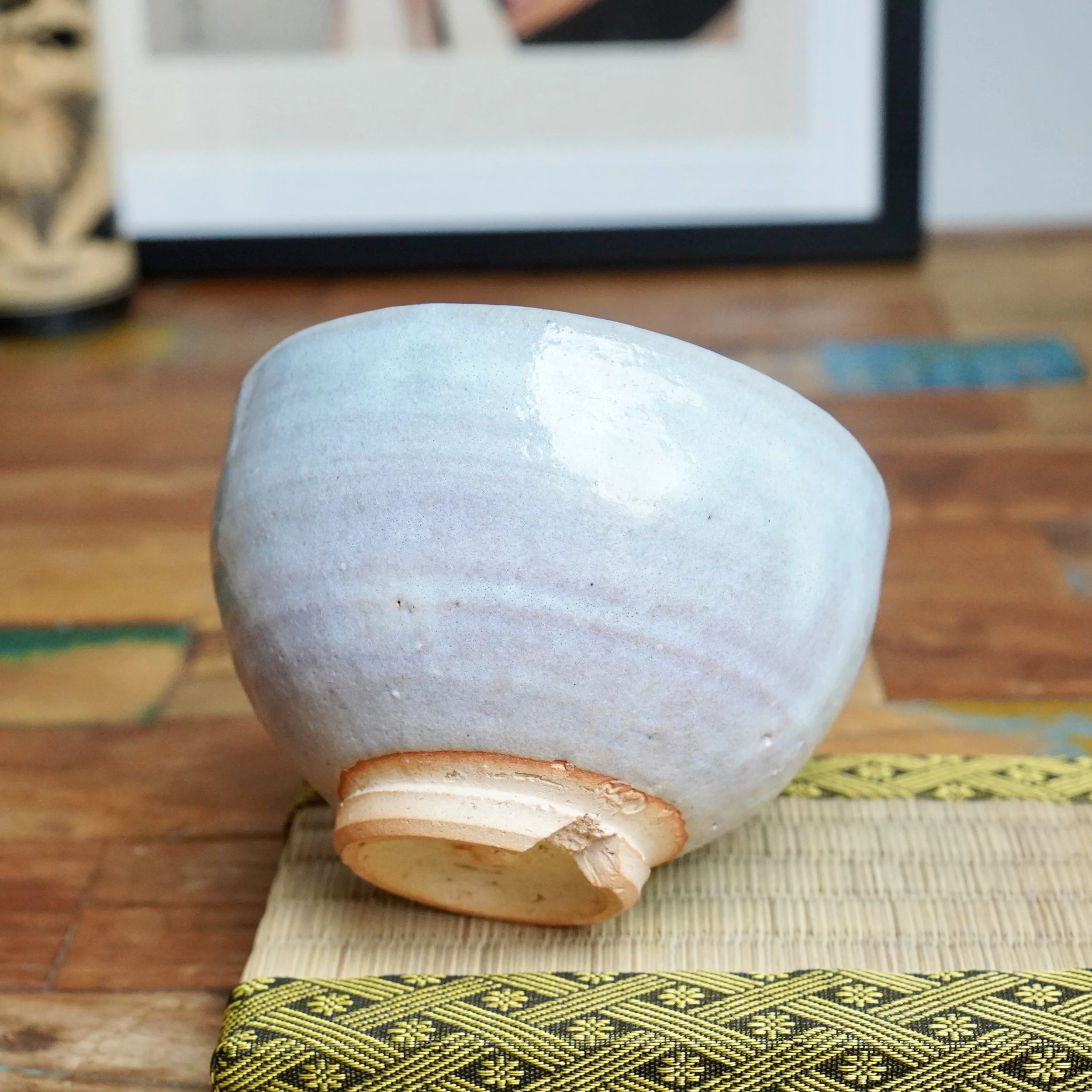 Moriwaki Fumitada chawan, glazed in soft white, blue-grey, and pale lilac, with an unglazed warikodai foot, resting on a woven mat.
