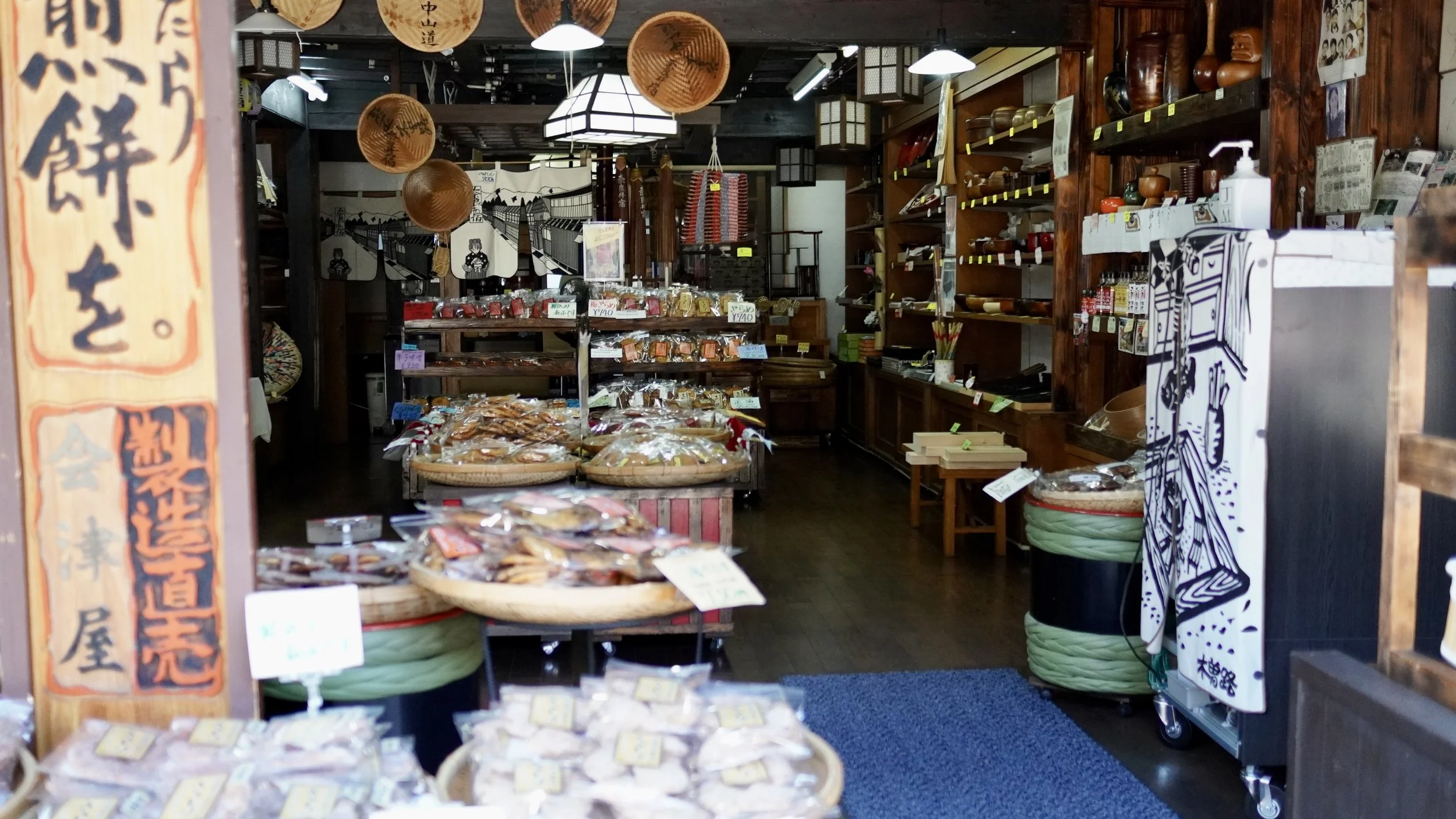 The interior of a traditional shop in Japan with wooden shelves filled with a variety of woven baskets, handmade pottery, and vintage household items sourced for the collection.