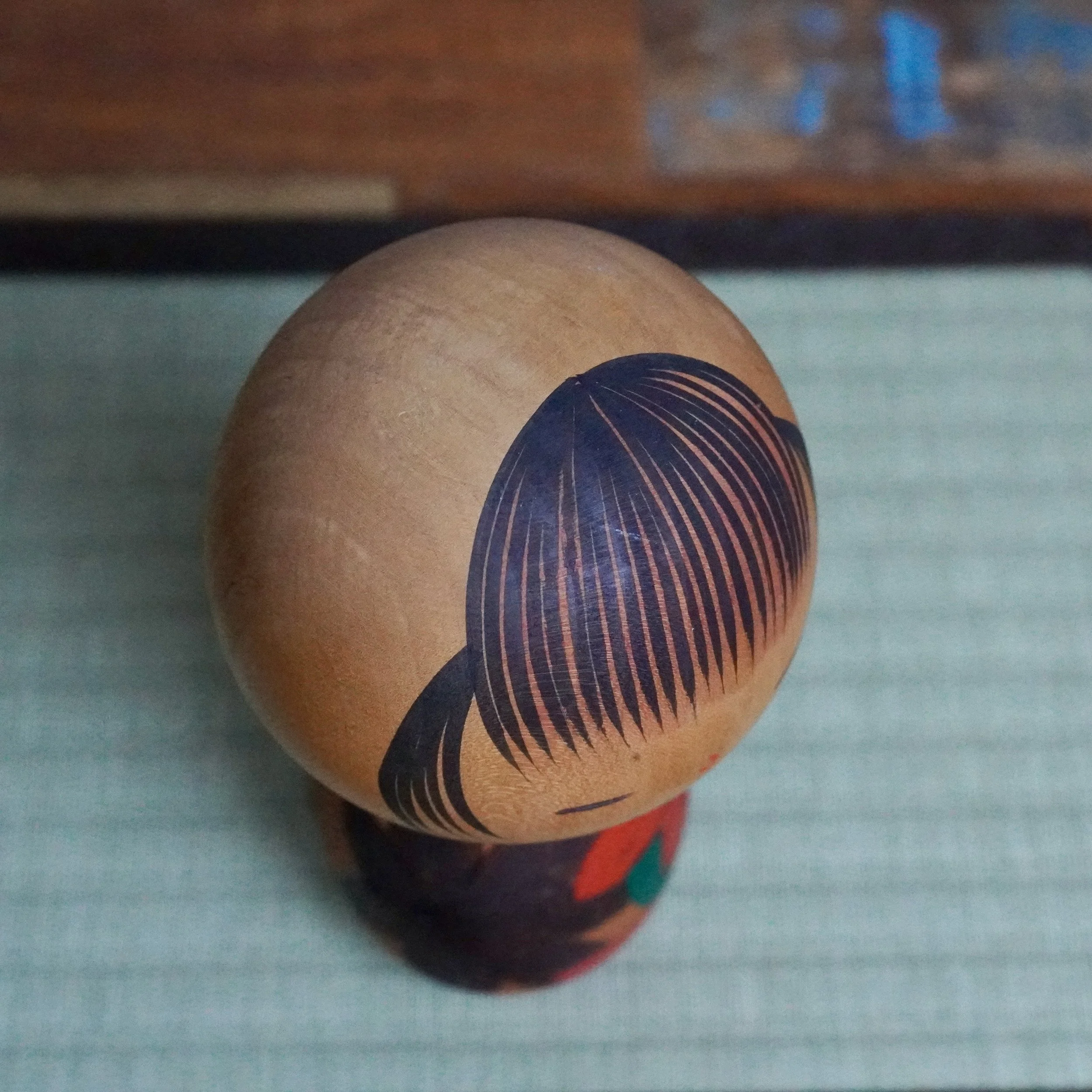 Yuji Kawase kokeshi with a natural wood head featuring black painted hair, top-down view. The dark, patterned body below shows carved red and deep-toned momiji leaves.