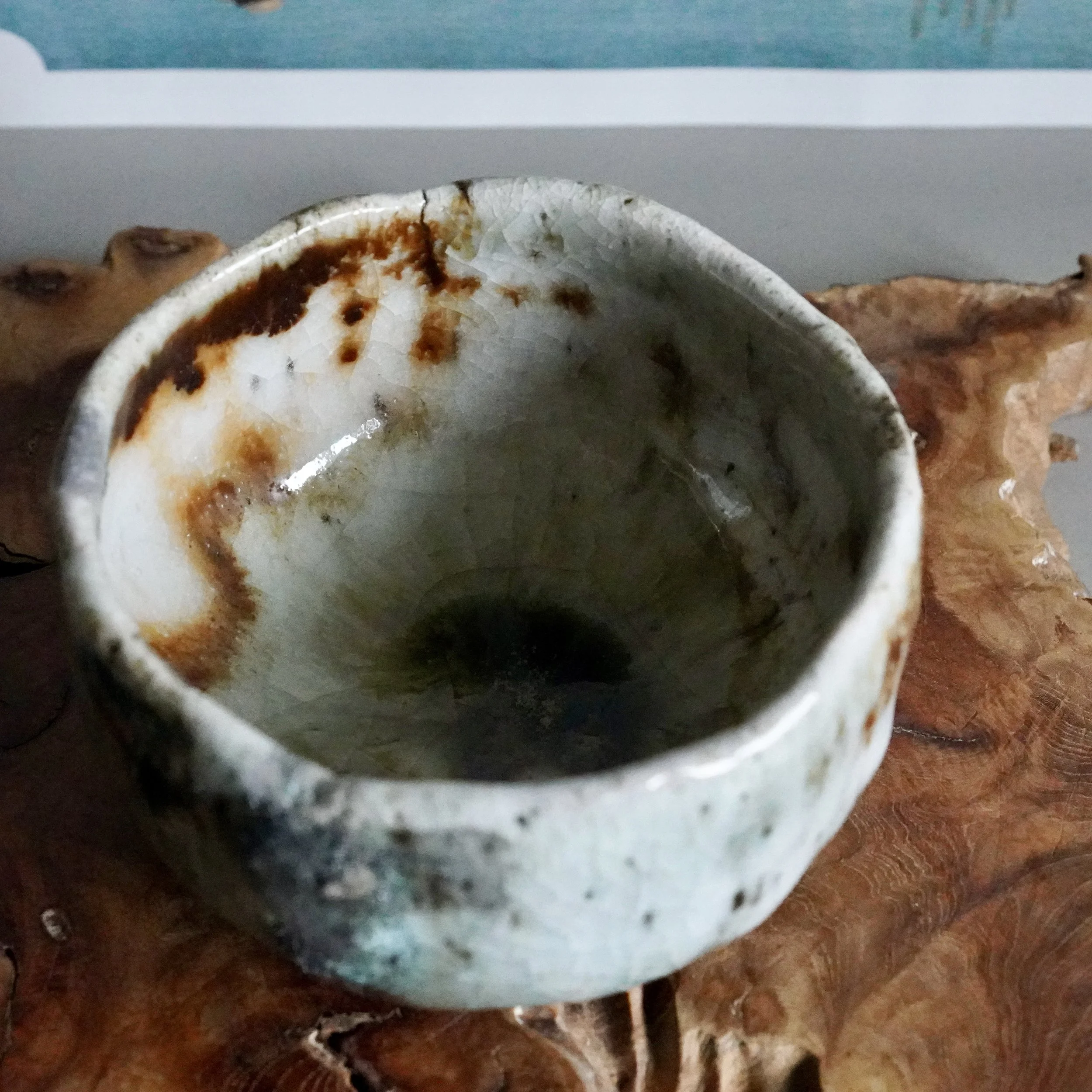 Deguchi Eiji chawan with crackled white, rust-brown, and blue-green glaze, deep green pooling in its interior, on a wood surface.