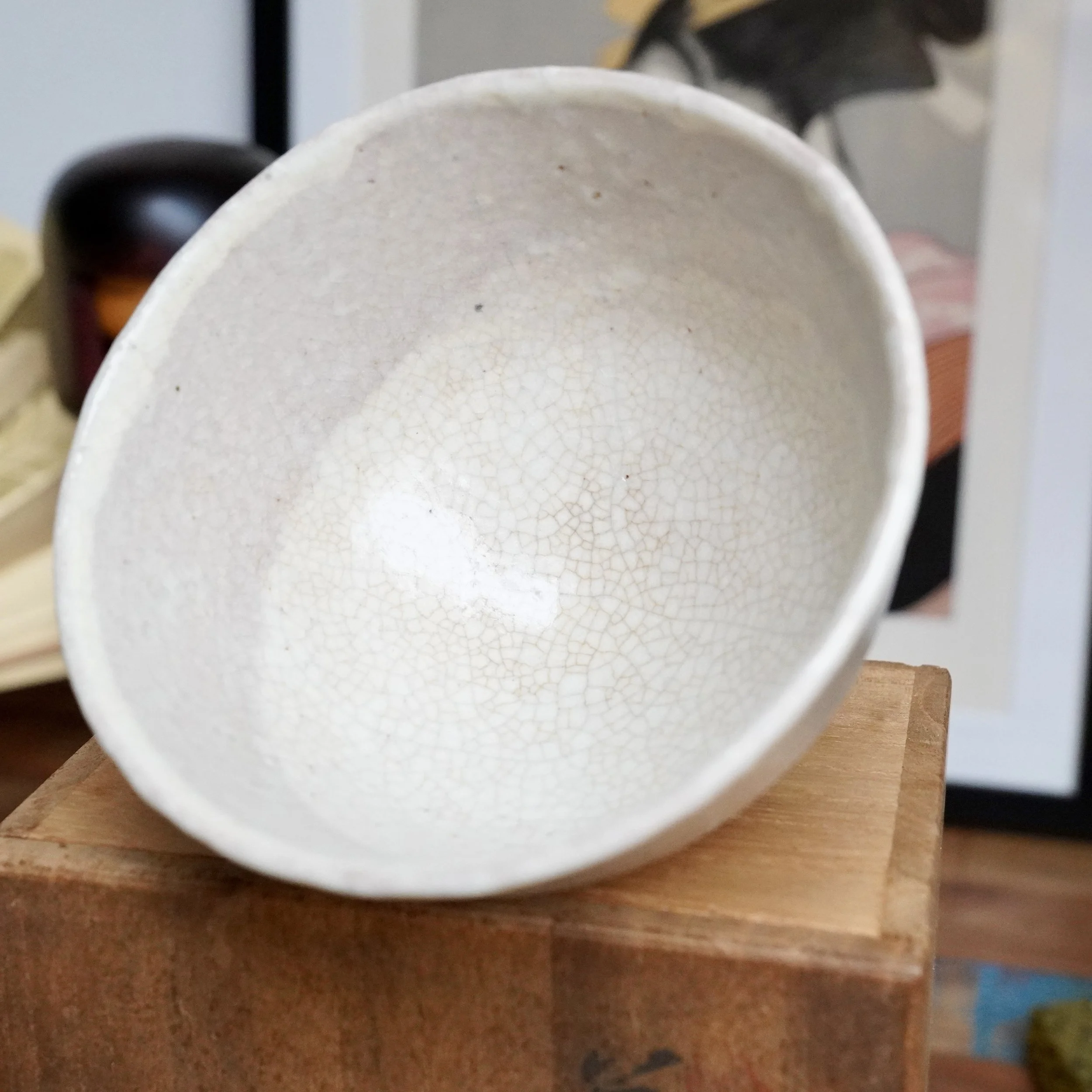 White Hagi-yaki chawan, interior seen from above, revealing a fine, dense, tea-stained crackle glaze. It rests on a light brown wooden surface. Tamamura Shōgetsu.