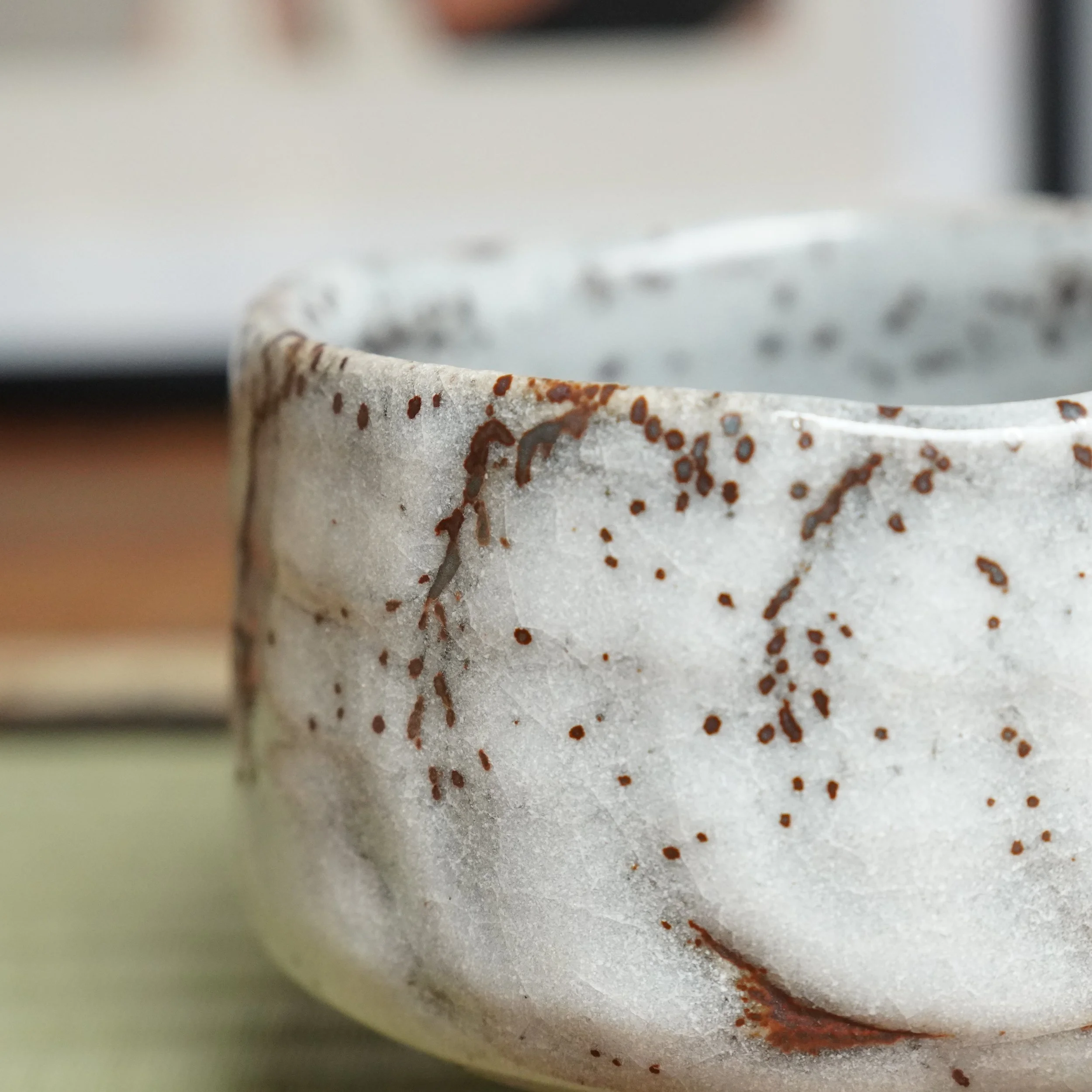 Oni-Shino chawan by Katō Shōzan, close-up. Thick white glaze with rust-brown speckles, drips, and visible crazing on its textured, indented surface.