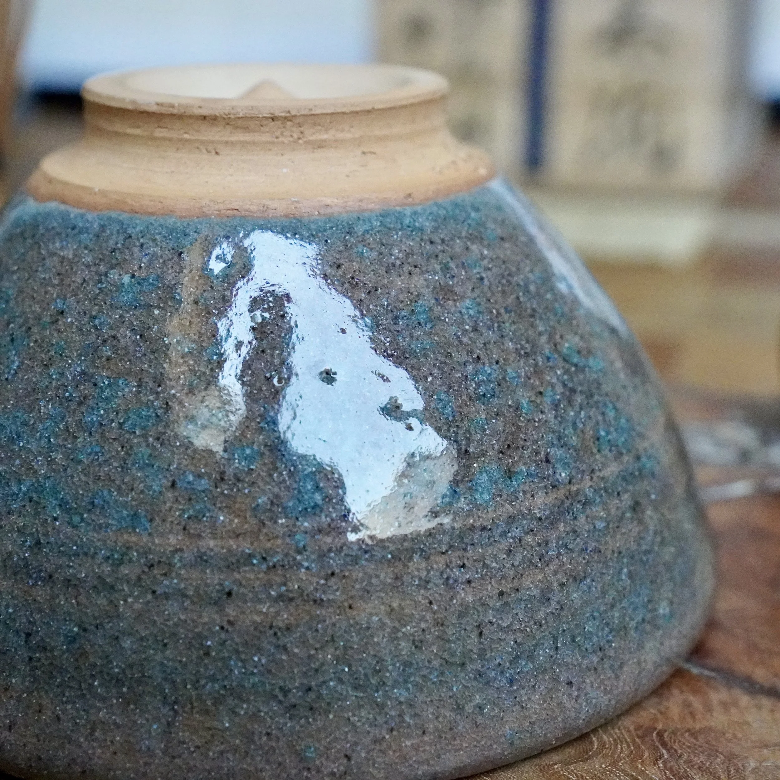 Angled close-up of an upside-down chawan by Mizushima Jirō, showing its unglazed light brown foot and a blue-speckled, glossy dark stoneware body with a bright reflection.