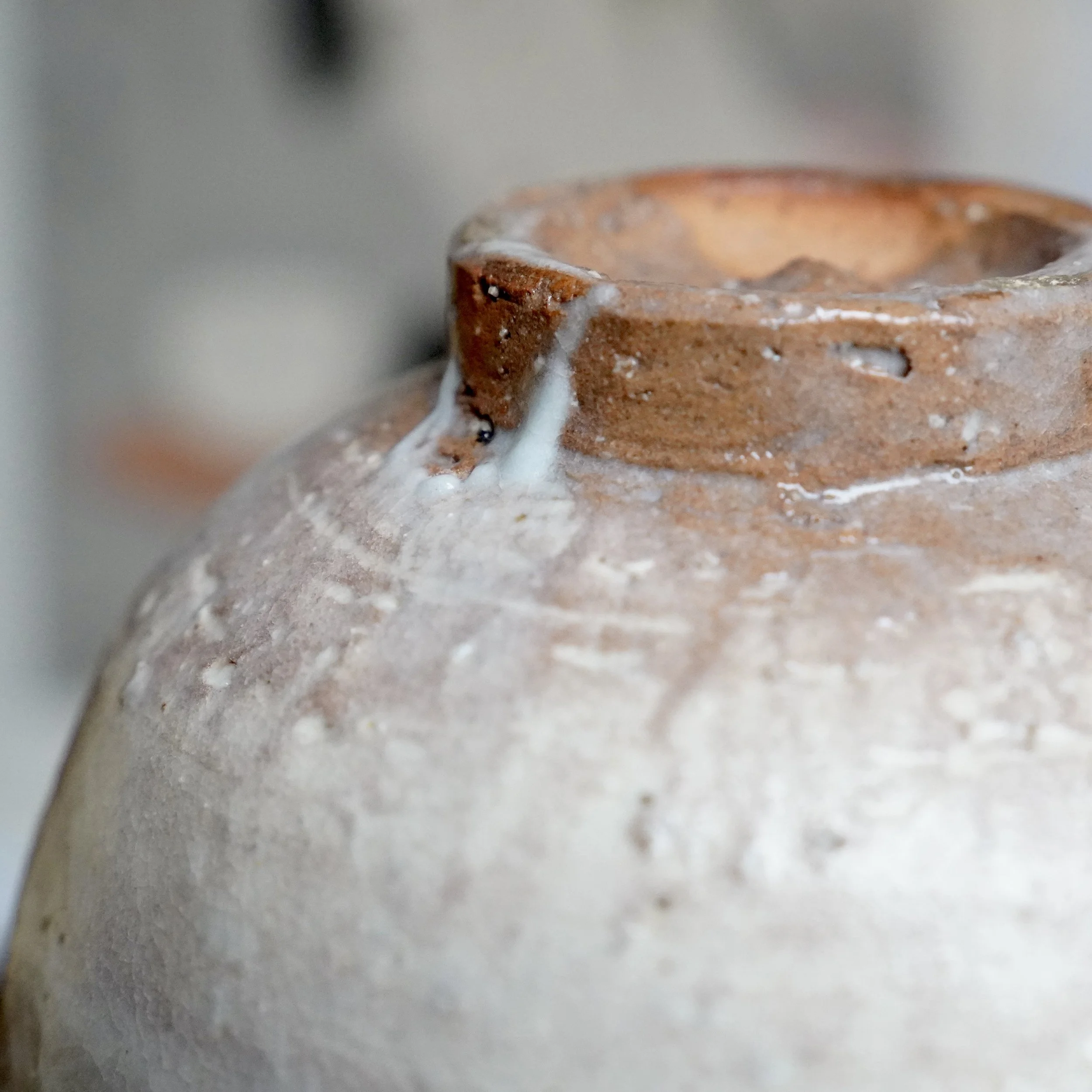 Close-up of a Hagi-yaki chawan by Tamamura Shōgetsu, showing a reddish clay rim with uneven white glaze dripping down its rough, textured body.