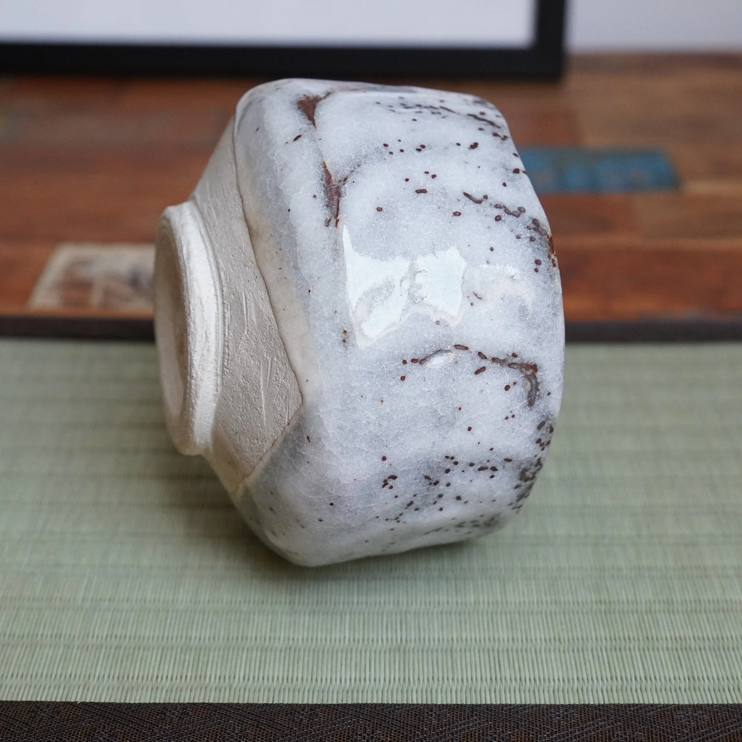 Katō Shōzan's oni-Shino chawan on its side, with a thick white crackled glaze and rust-brown flecks and drips highlighting its indented outer wall.