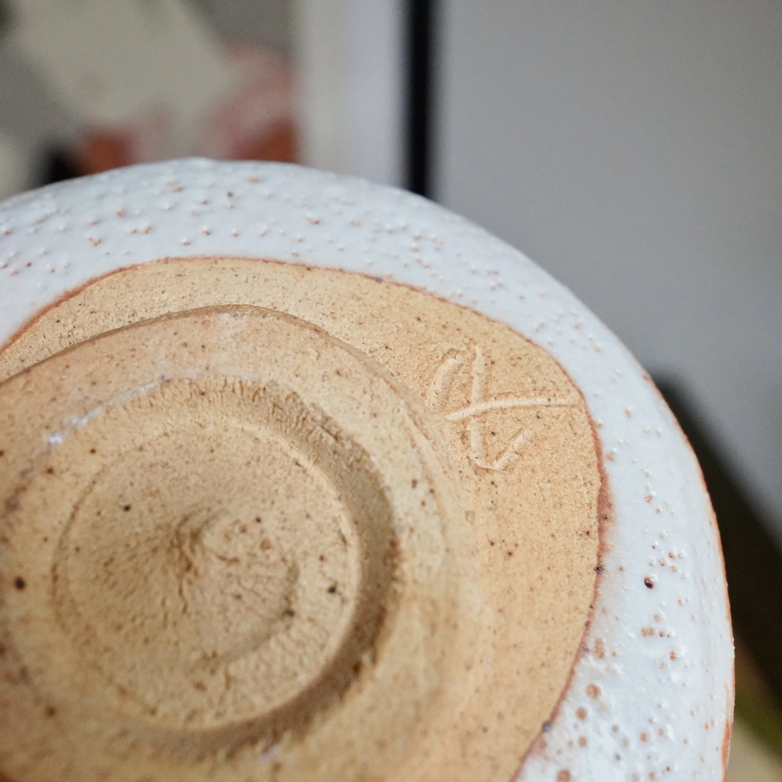 Bottom of a ceramic chawan, featuring an unglazed footring with a carved signature and a textured white-and-orange speckled glaze.