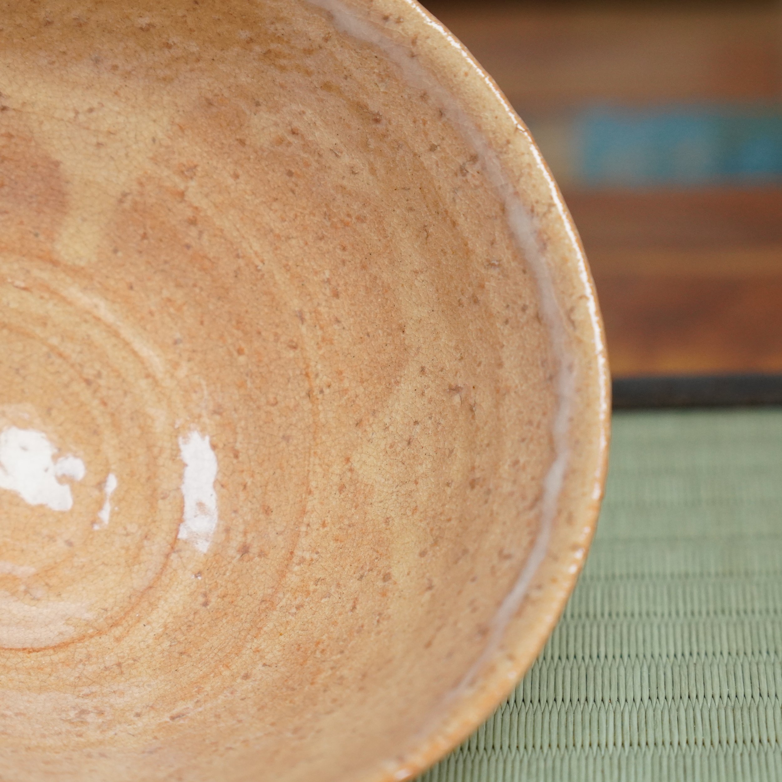 Hagi-yaki chawan by Kaneko Nobuhiko, revealing its crackled salmon-apricot interior with dark speckles and white rim glaze. Blurred tatami mat in background.
