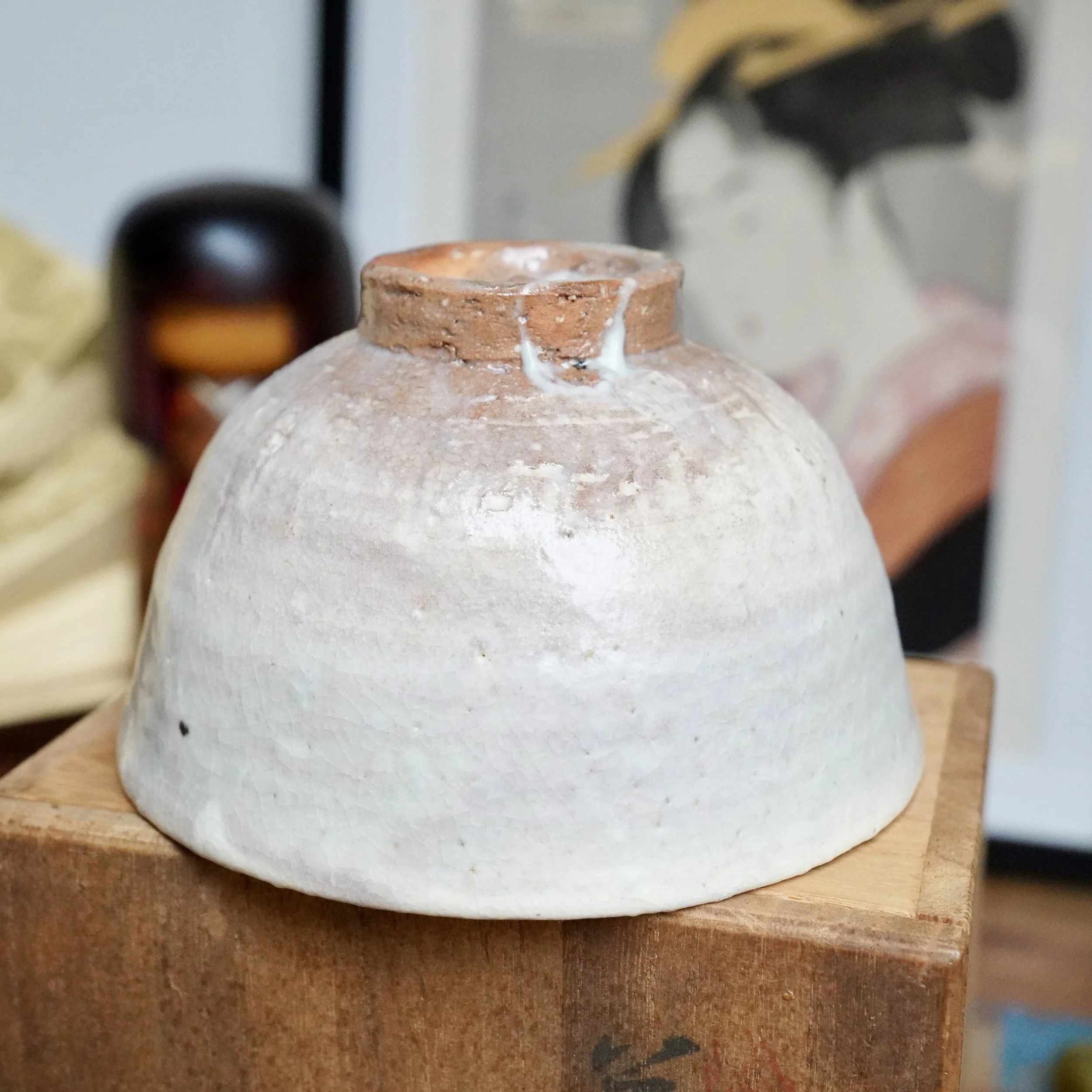 Hagi-yaki chawan by Tamamura Shōgetsu, upside-down, with an off-white crackle glaze fading into a reddish-brown clay rim, set on a wooden box.