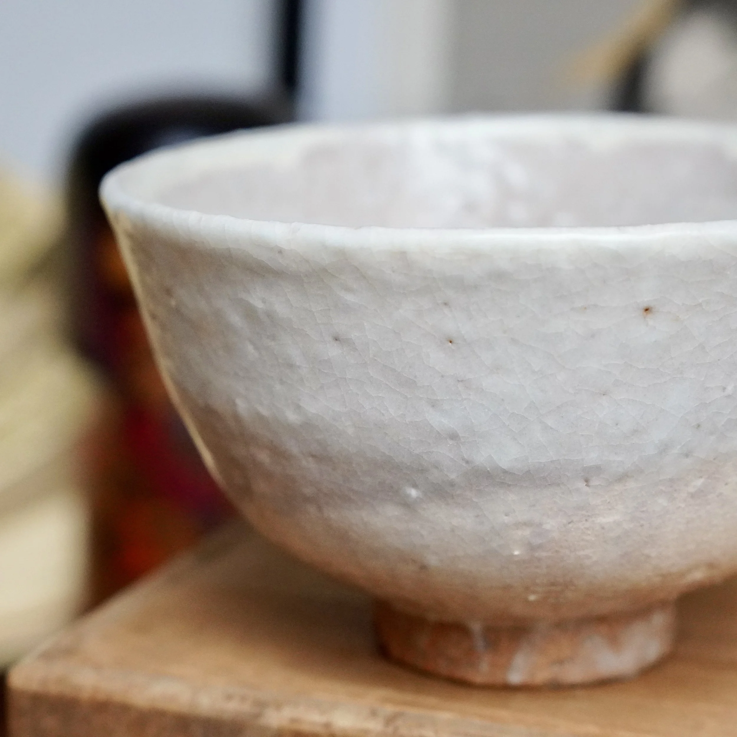 White crackled Hagi-yaki chawan by Tamamura Shōgetsu, showing dense glaze crackle and subtle tea stains, with a visible reddish clay foot on wood.