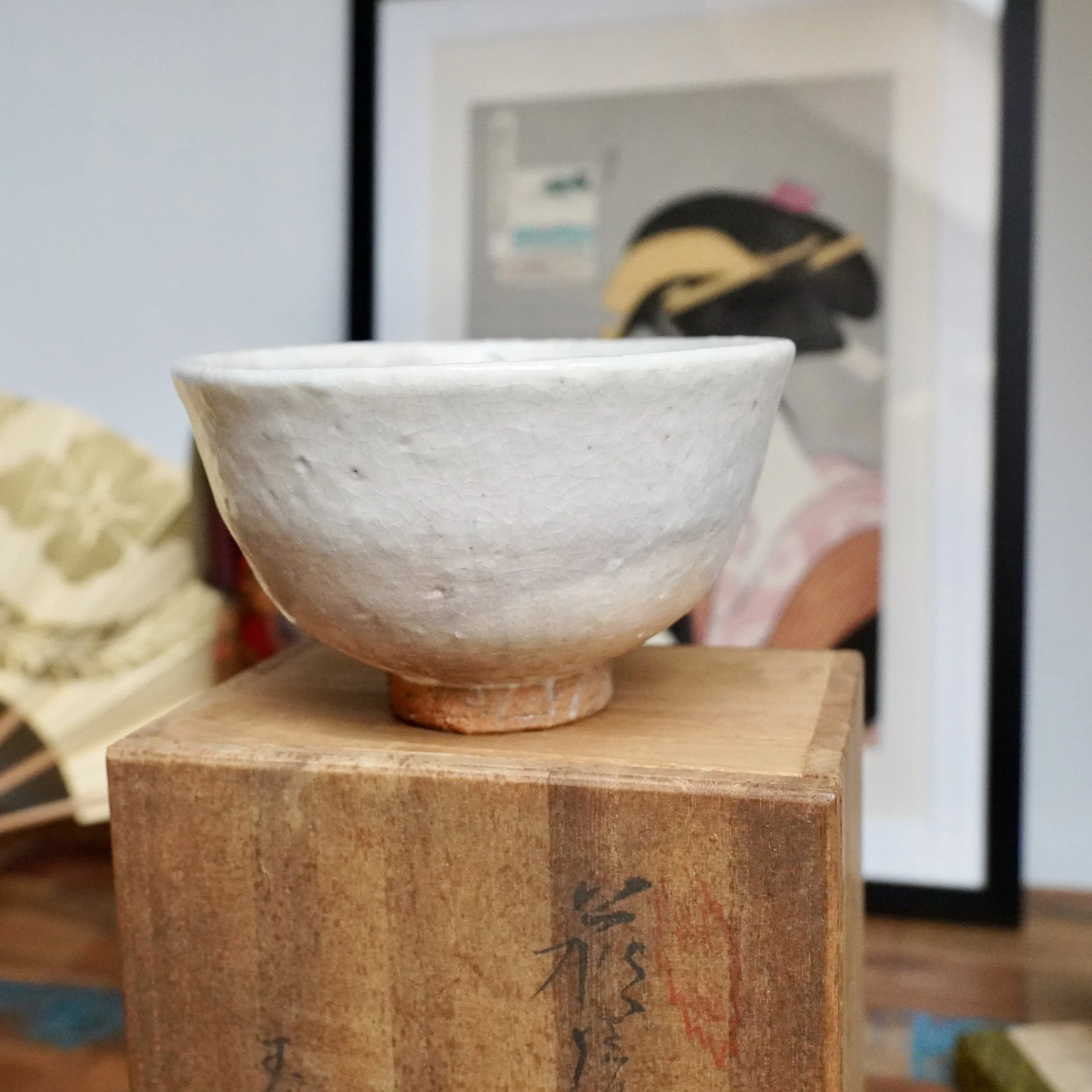 Tamamura Shōgetsu chawan, white crackled glaze transitions to reddish unglazed clay at the foot, resting on a wooden storage box.