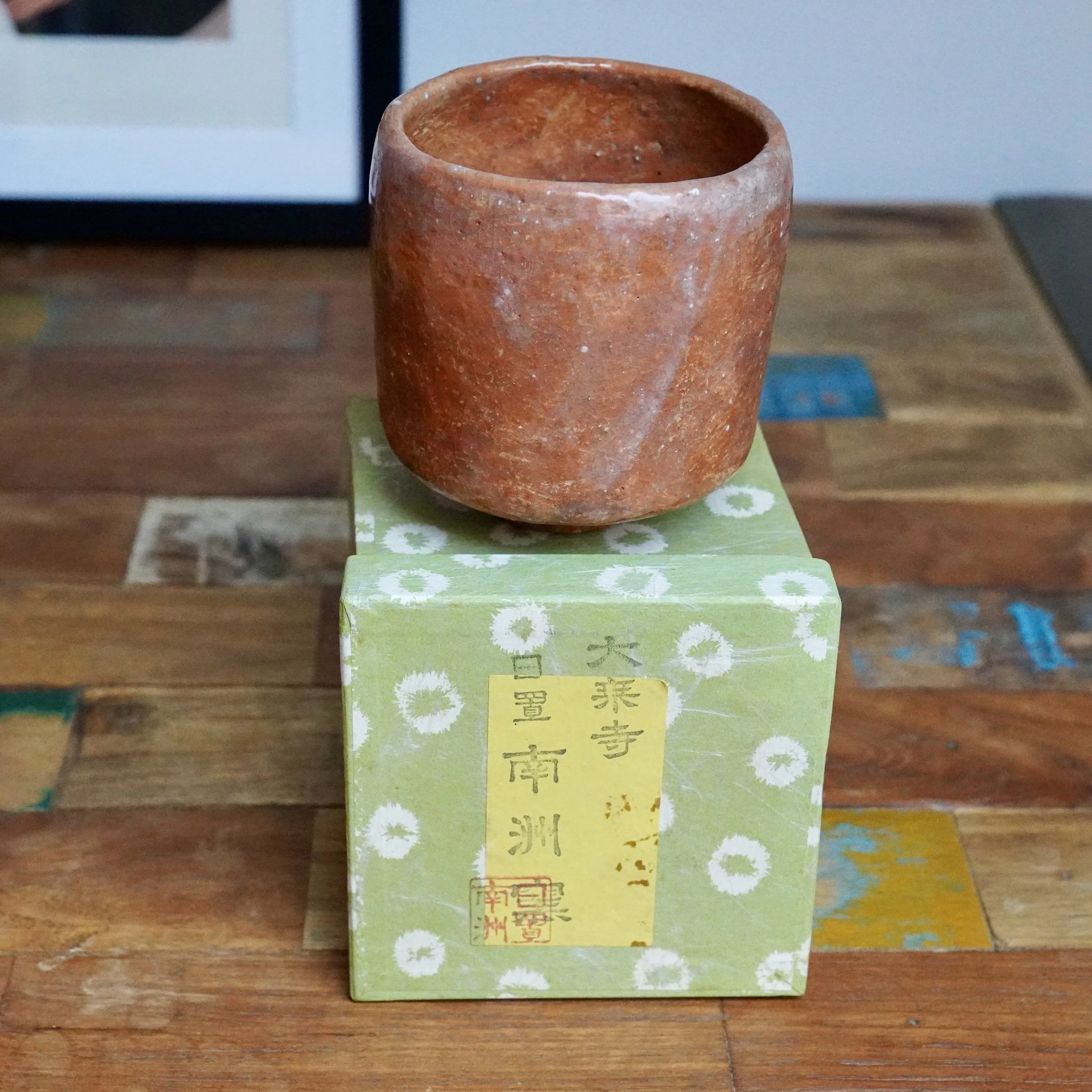 Terracotta-colored tsutsu chawan with white drip glaze and textured finish, displayed on a green box with Japanese script, marked by Hioki Nanshū kiln.