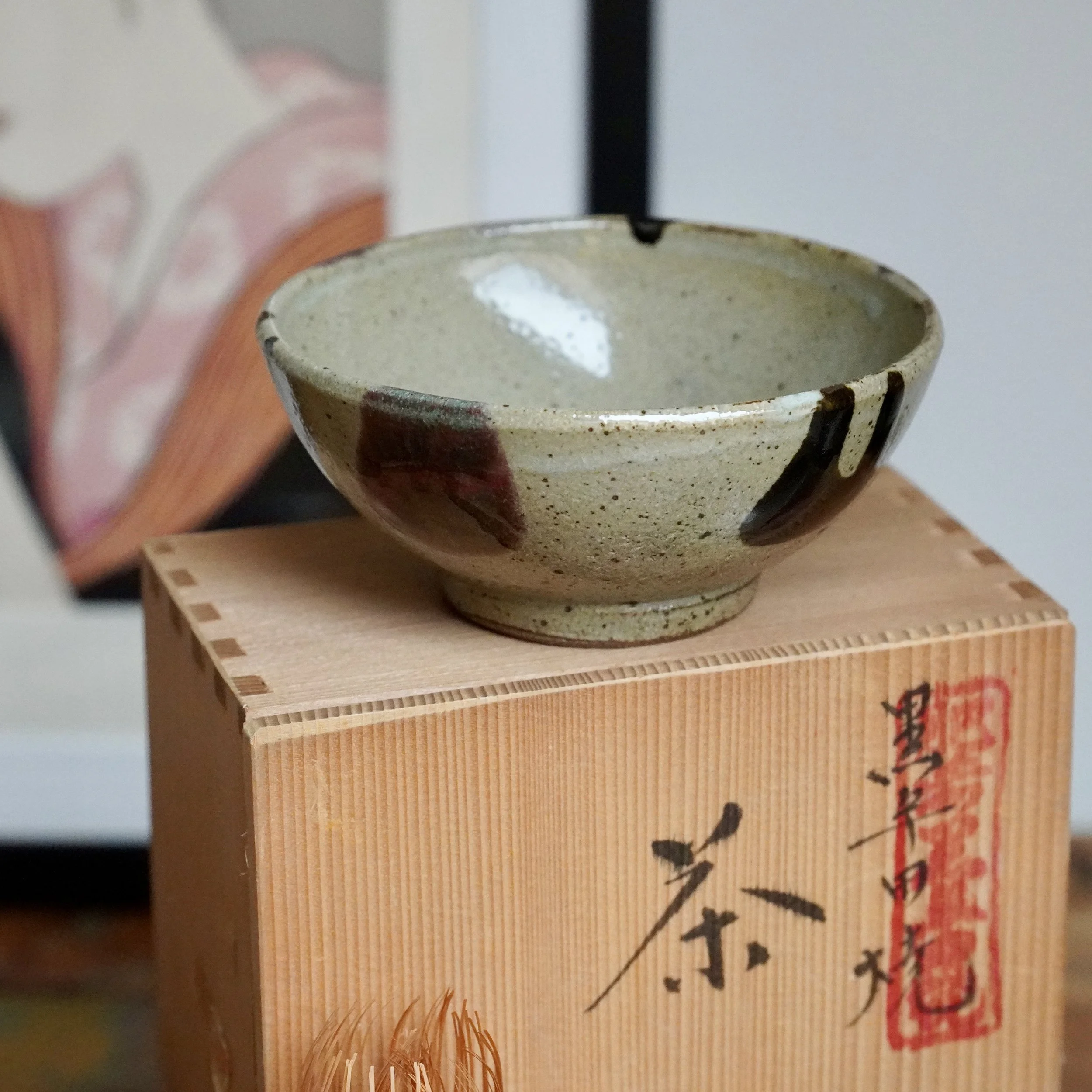 Kuromuta-yaki hira-chawan with speckled glaze, dark strokes, and reddish patches, on a wooden tomobako with Maruta Nobumasa kiln calligraphy and red seal.