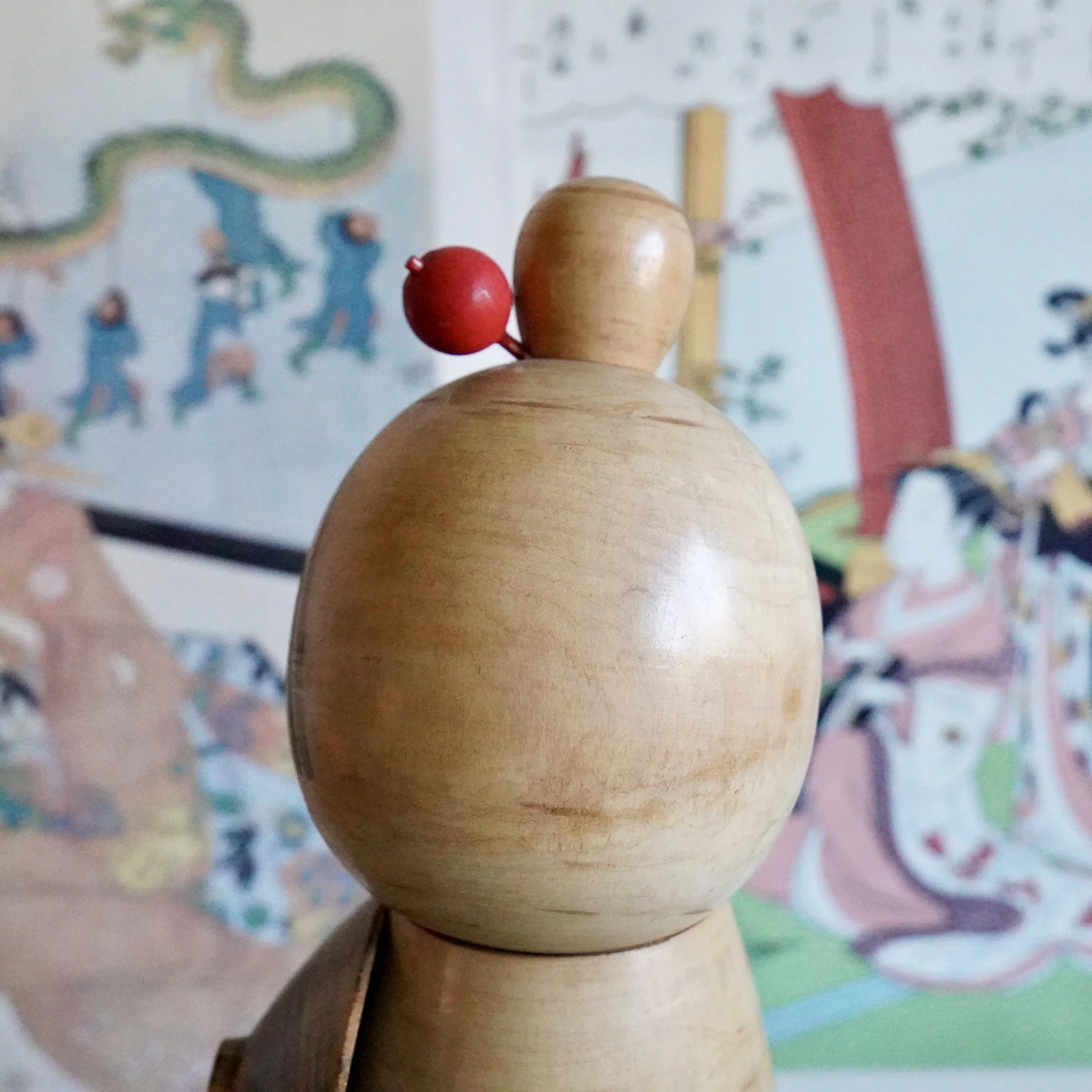 Overhead view of Sato Suigai sōsaku kokeshi, red wooden hair bead and striped crown