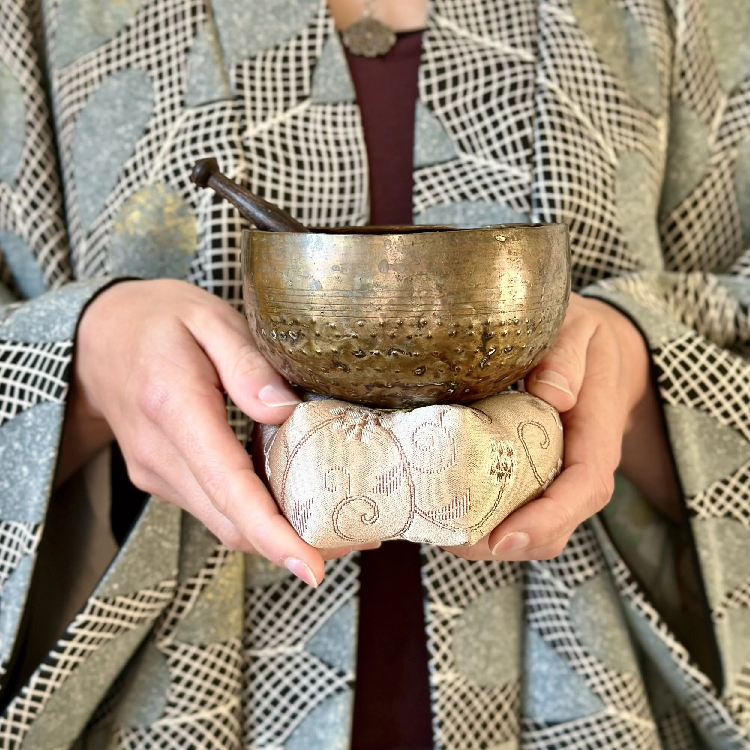 Antique Japanese orin singing bowl, hammered bronze with dark patina, held in hands with wooden striker and kimono haori on background