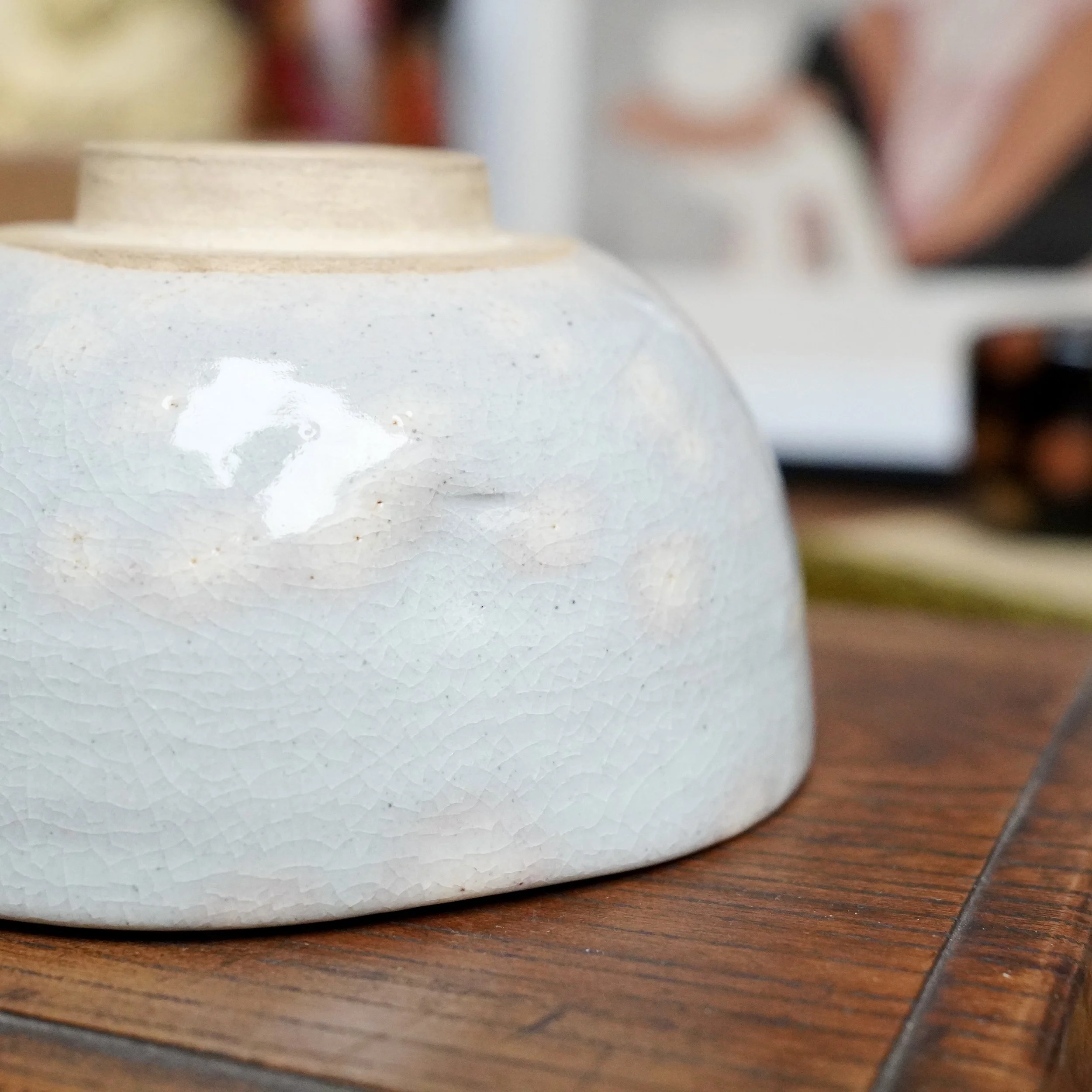 Izushi ware chawan by Nagasawa Minoru, featuring a grey-blue crackled glaze with a faint pink blush, resting on a wooden surface.