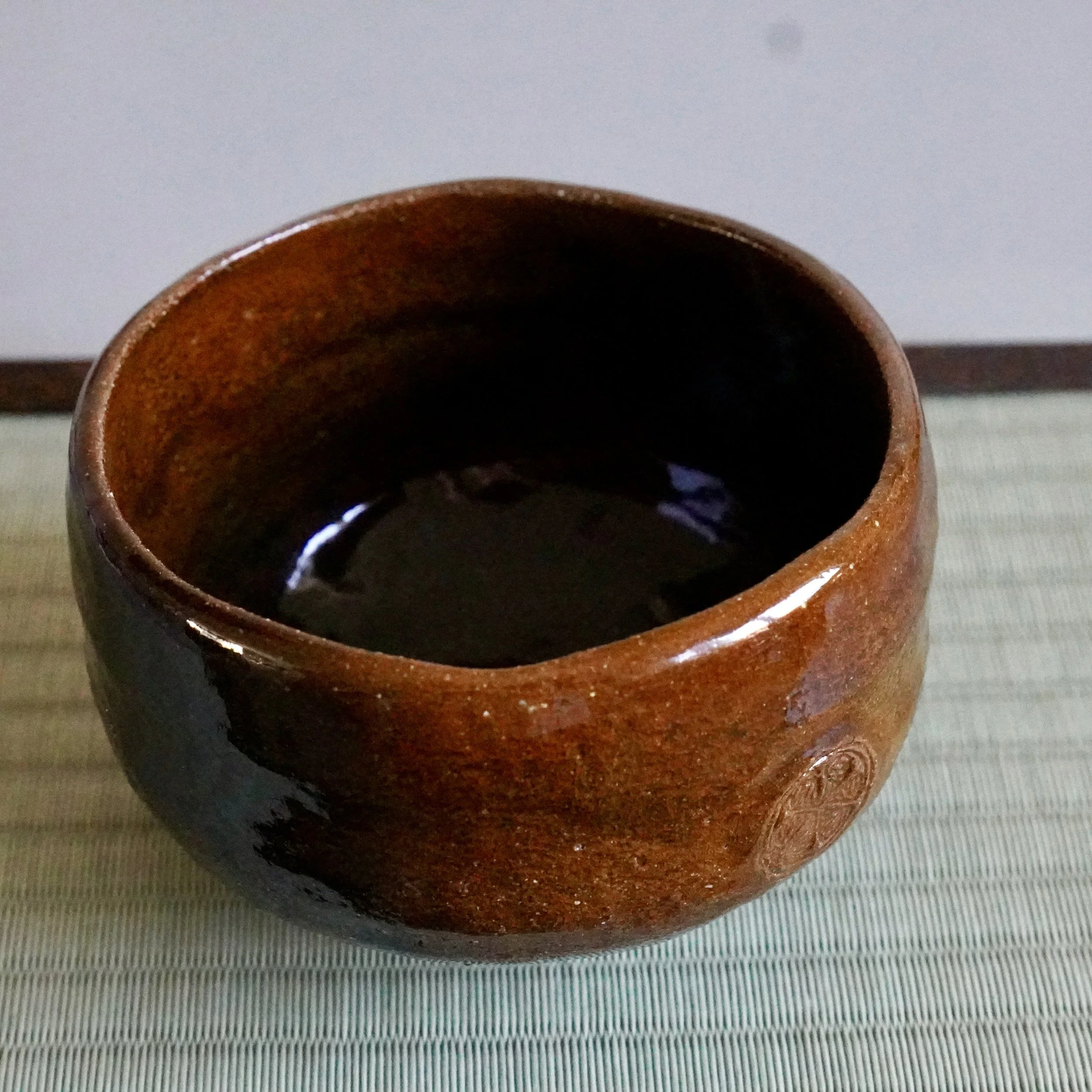 Ōbi-yaki chawan on a tatami mat showing the ame-yu glaze shifting from amber to near-black inside the bowl