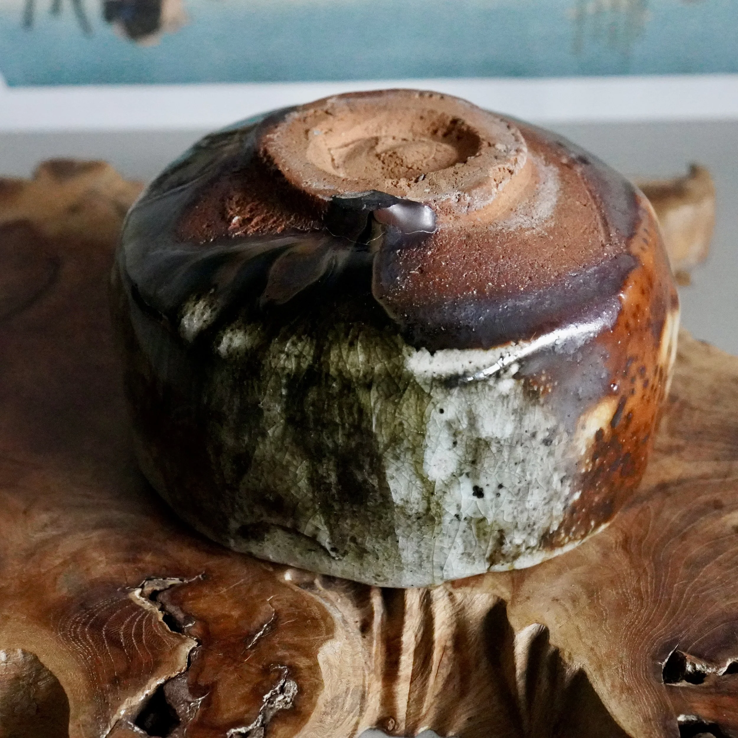 Wood-fired chawan by Deguchi Eiji, revealing an unglazed reddish foot, dark brown to rust glaze, and crackled white-green lower body, on textured wood.