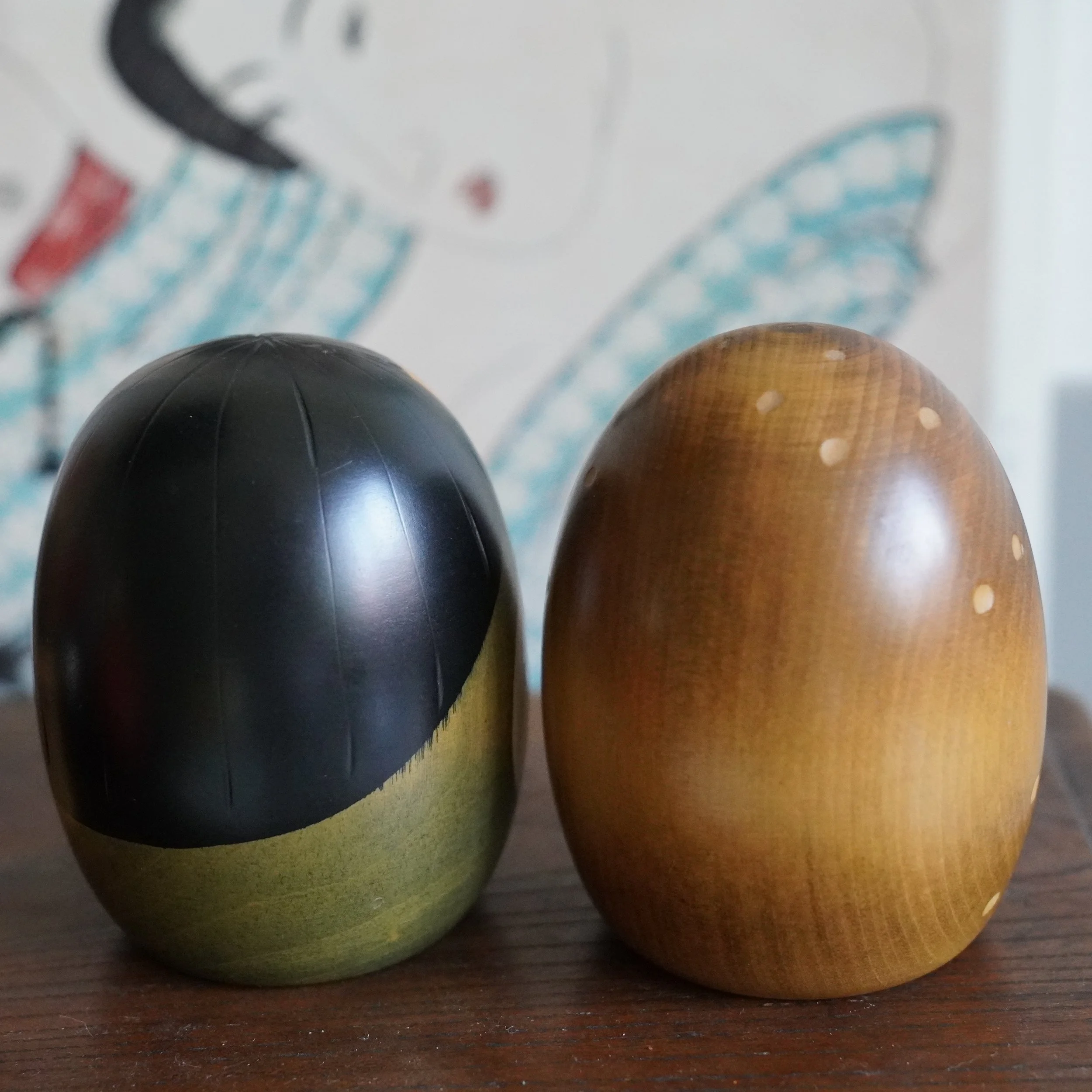 Close up of vintage Usaburo kokeshi pair, black lacquered crowns, wave motif and honey toned wood, Showa period