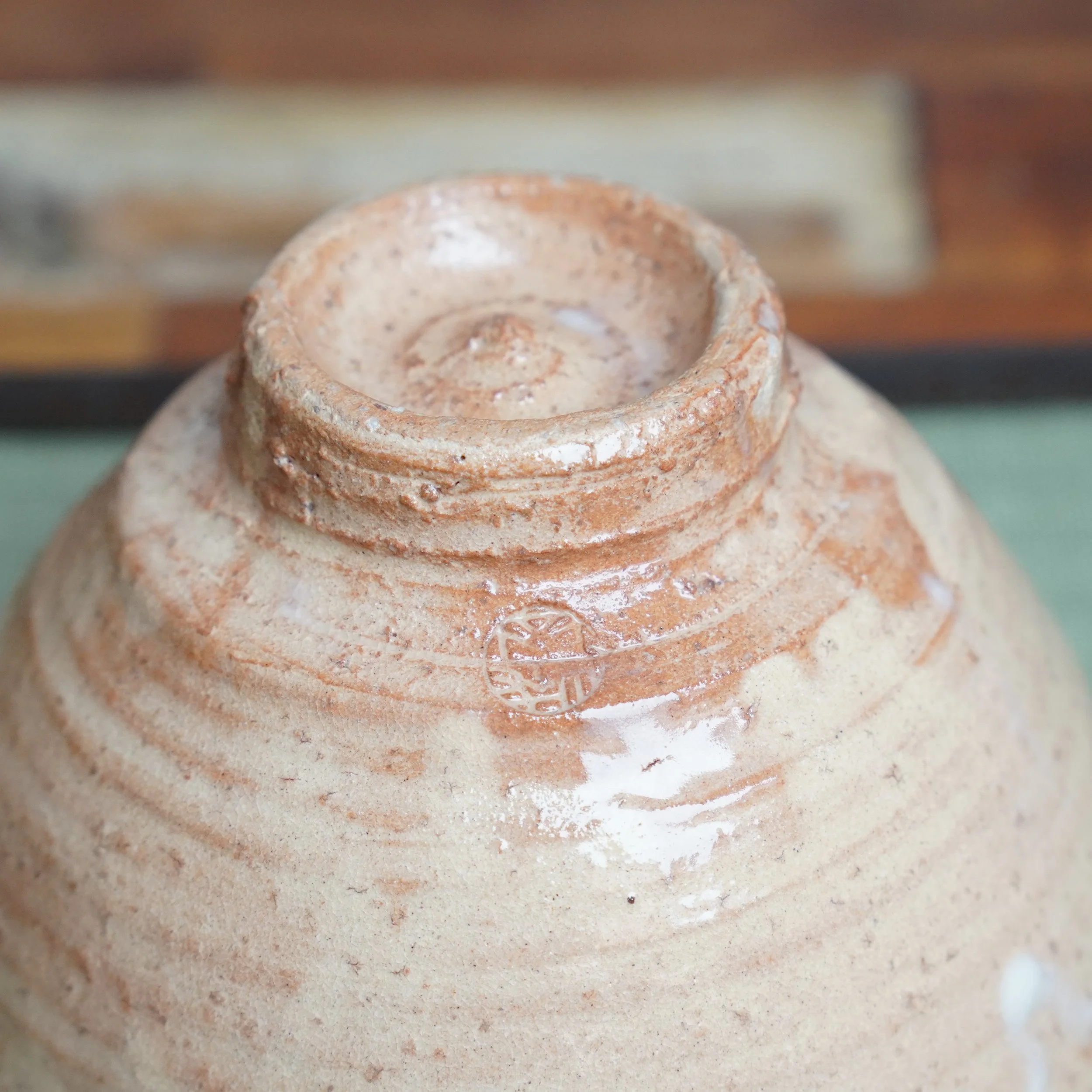 Underside of a Kaneko Nobuhiko Hagi-yaki chawan, with its tall foot, salmon-pink body, wheel marks, and an impressed signature beneath milky white glaze.