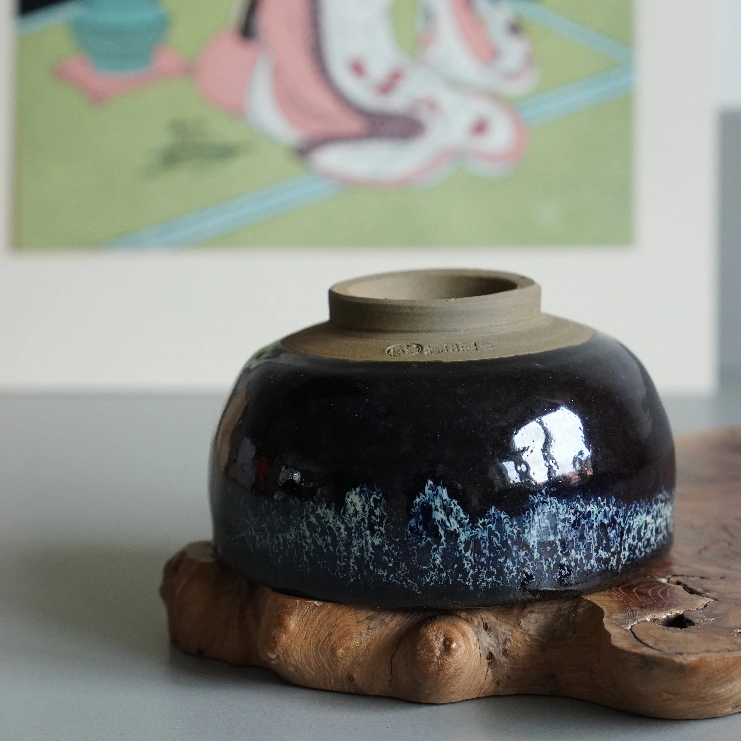 Rokuhō (鹿峰) signed dark brown matcha bowl with blue-white flowing glaze, unglazed foot, on a rustic wood stand.