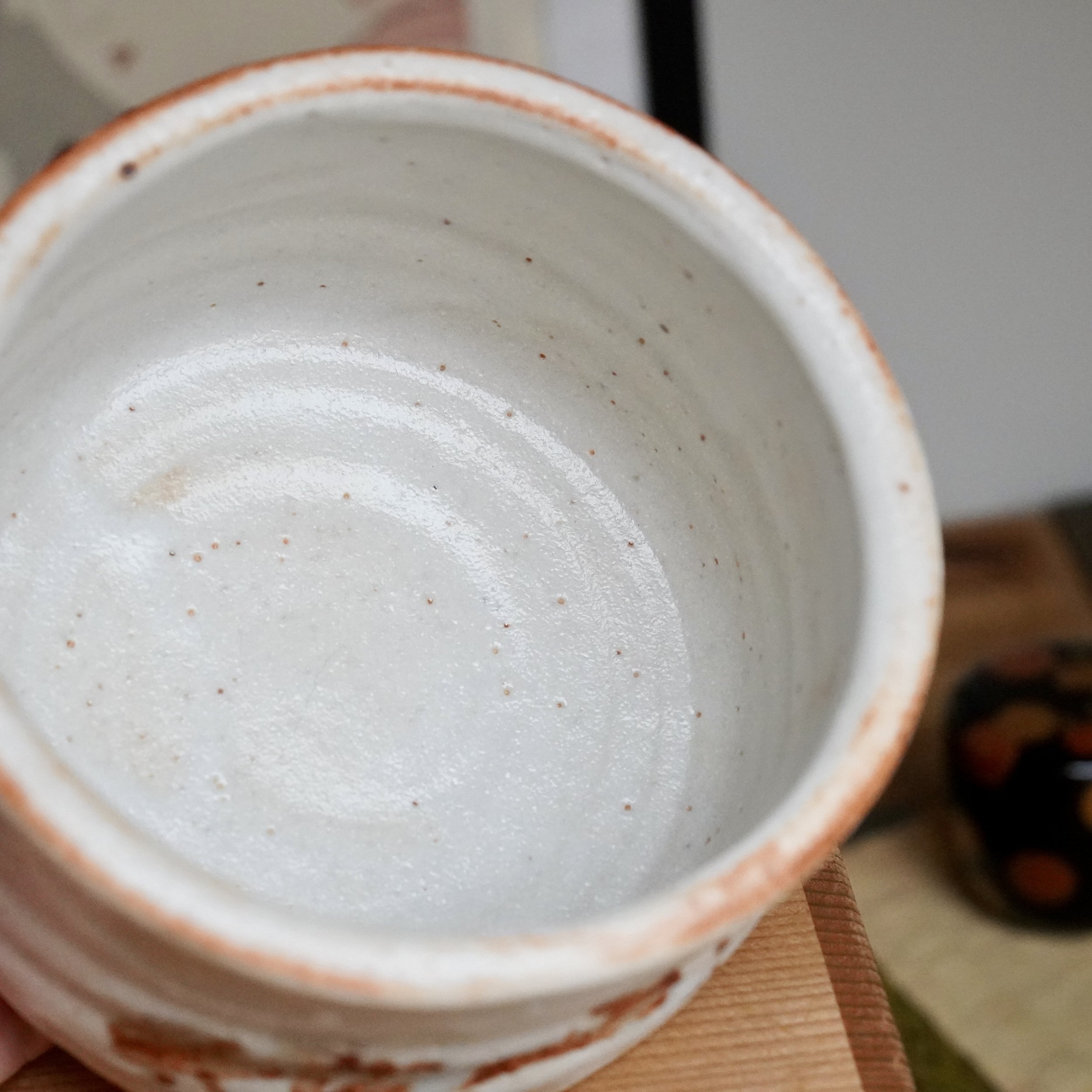 Interior of a creamy white Shino chawan, speckled with reddish-brown iron spots and an irregular rim with rust-orange blush.