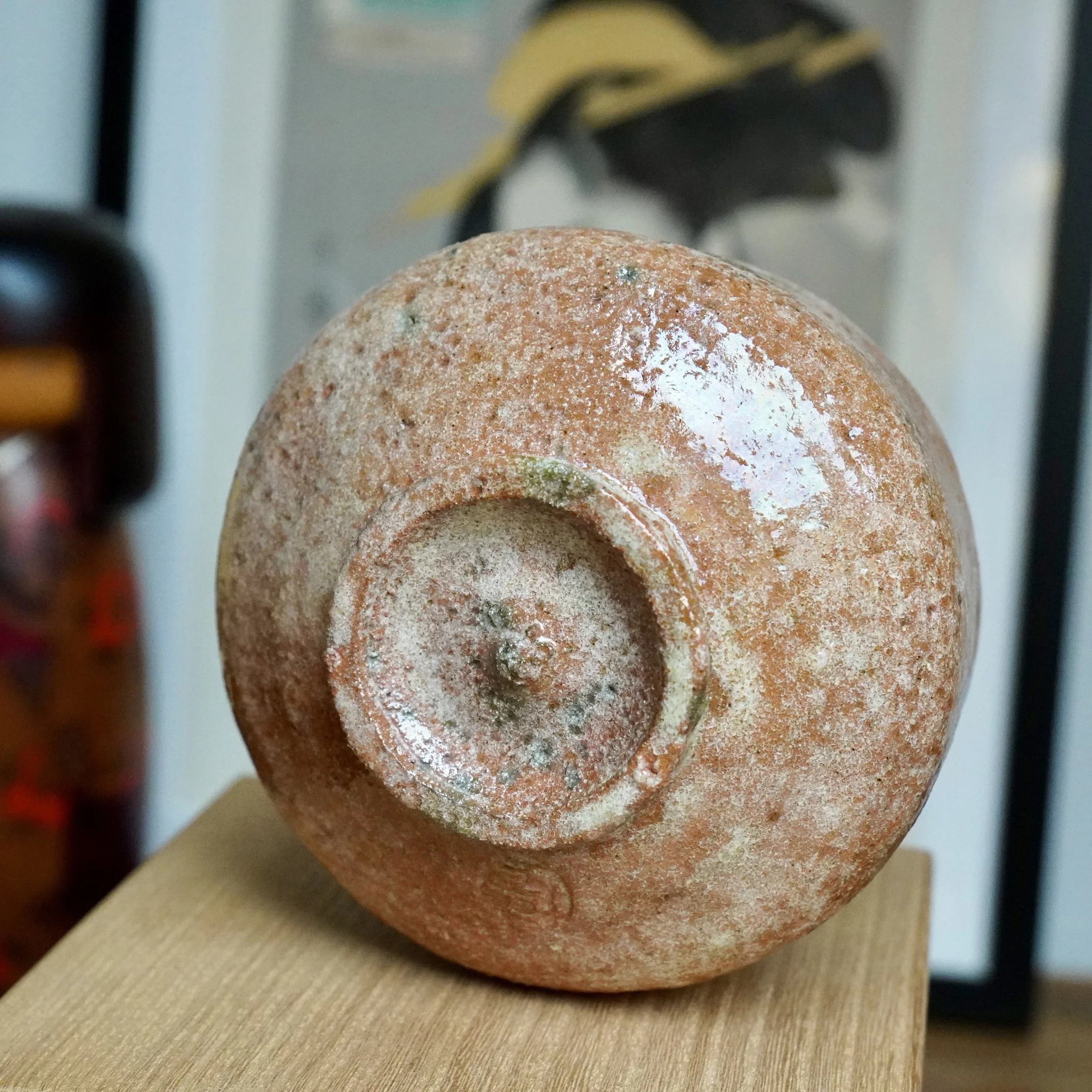 Underside of aka-raku chawan by Sawada Hiroyuki. Rugged, reddish-orange, sandy surface, glossy glaze patches and white drips. Circular foot, impressed signature.